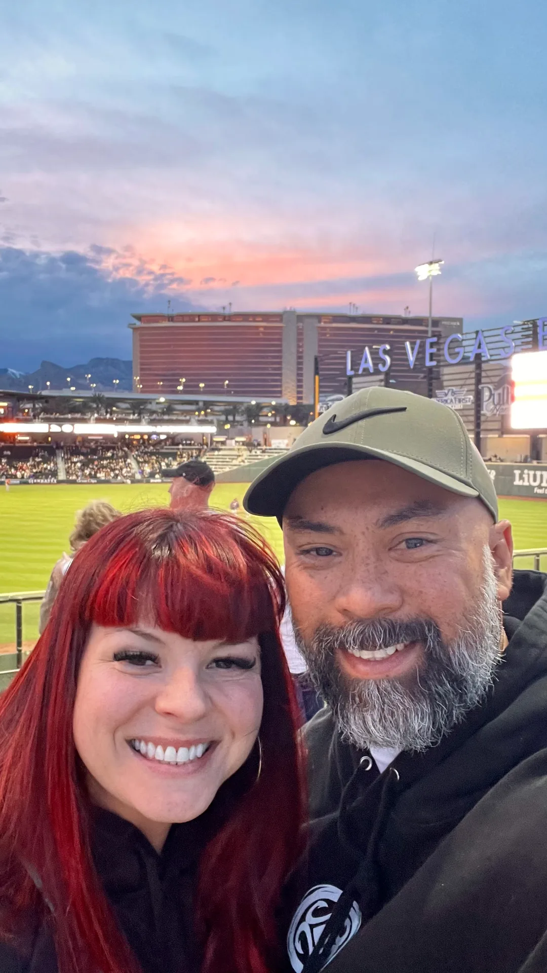 Samantha Medeiros and her husband at Las Vegas Ballpark with the LAS VEGAS sign and sunset sky behind them