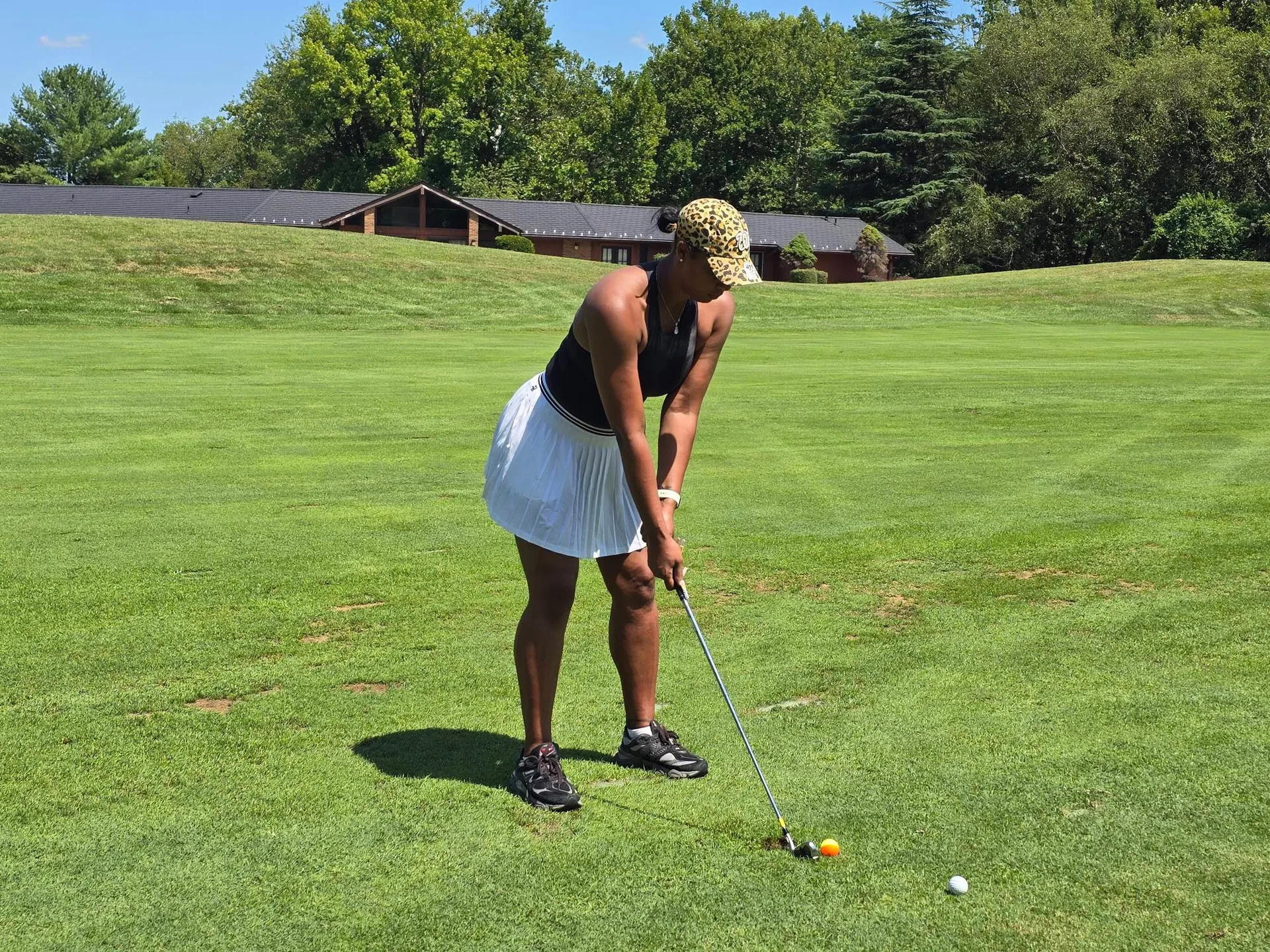 Woman in leopard-print cap addressing the ball on the fairway at the FORE the KIDS Golf Tournament