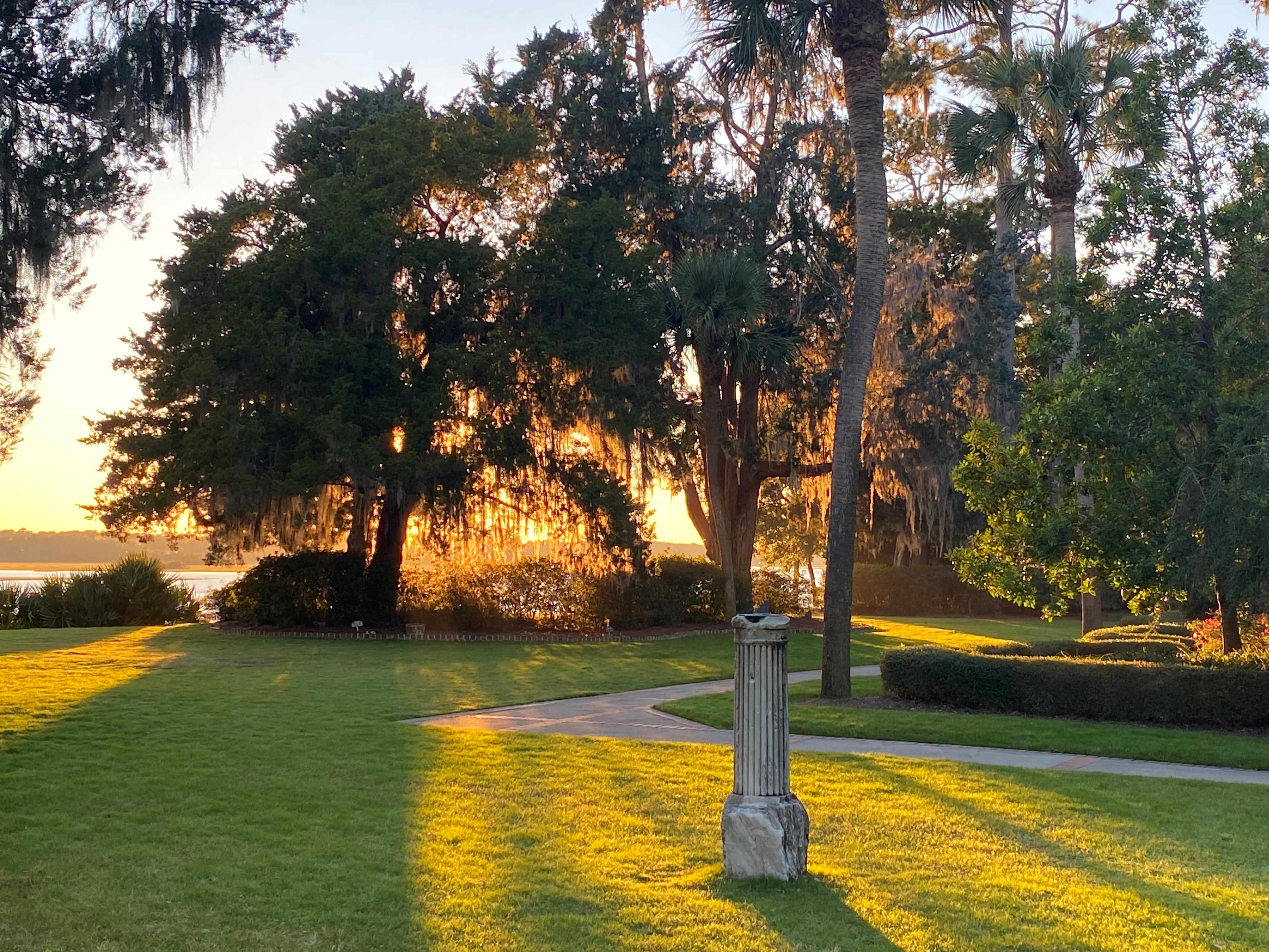 Landscaped lawn with a stone column at golden hour, portrait view of palms and Spanish-moss oaks