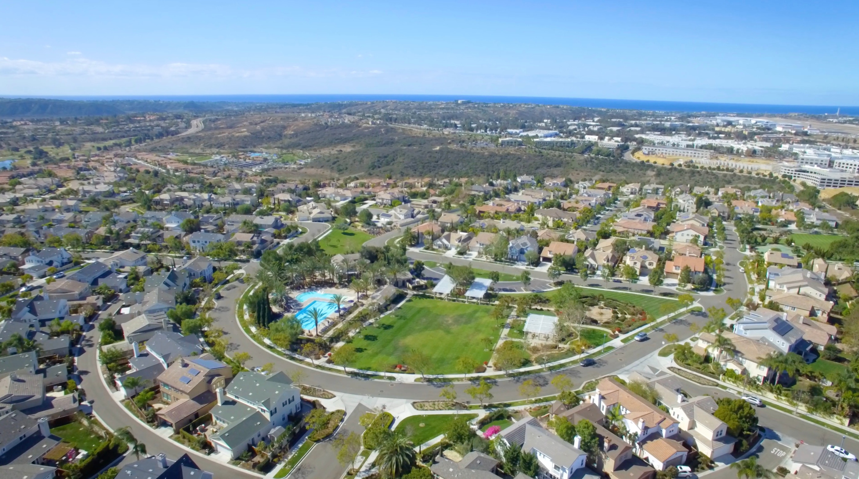 A modern walkable village center in Carlsbad at dusk with warm-lit townhomes around a landscaped square