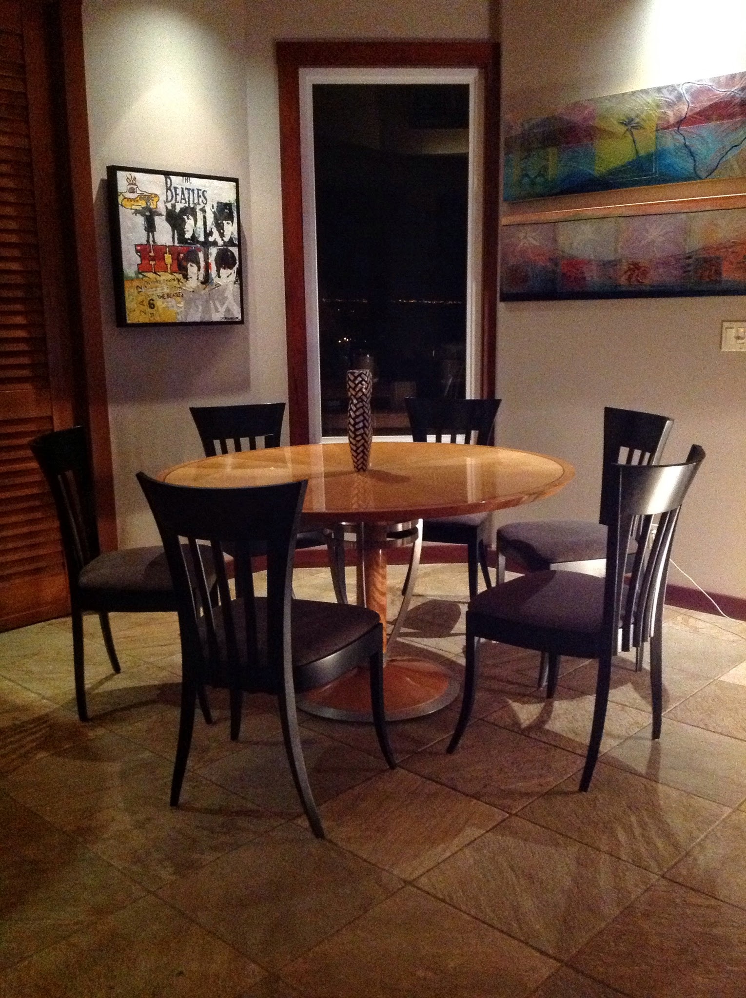 An oval wood dining table with a sculptural metal base, dark chairs, and paintings in Carol's home.