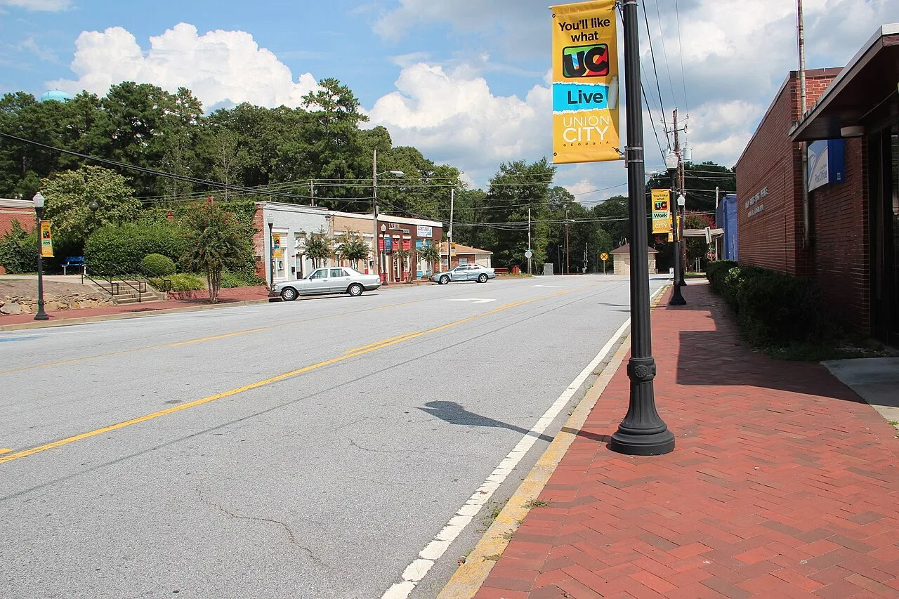 A sunny street scene in Union City with brick sidewalks, storefronts, trees, and a lamppost