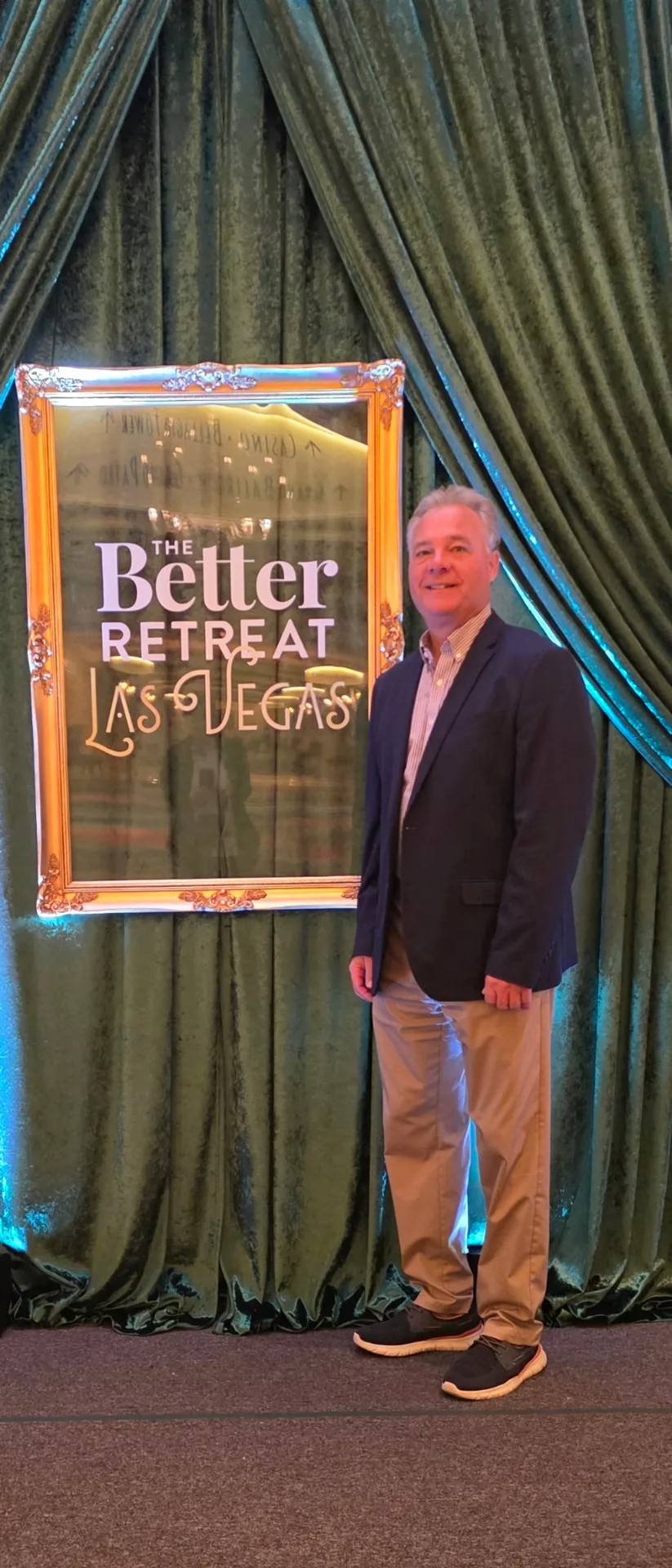 An attendee in a dark blazer stands in front of The Better Retreat Las Vegas sign at the Better Homes and Gardens Real Estate retreat
