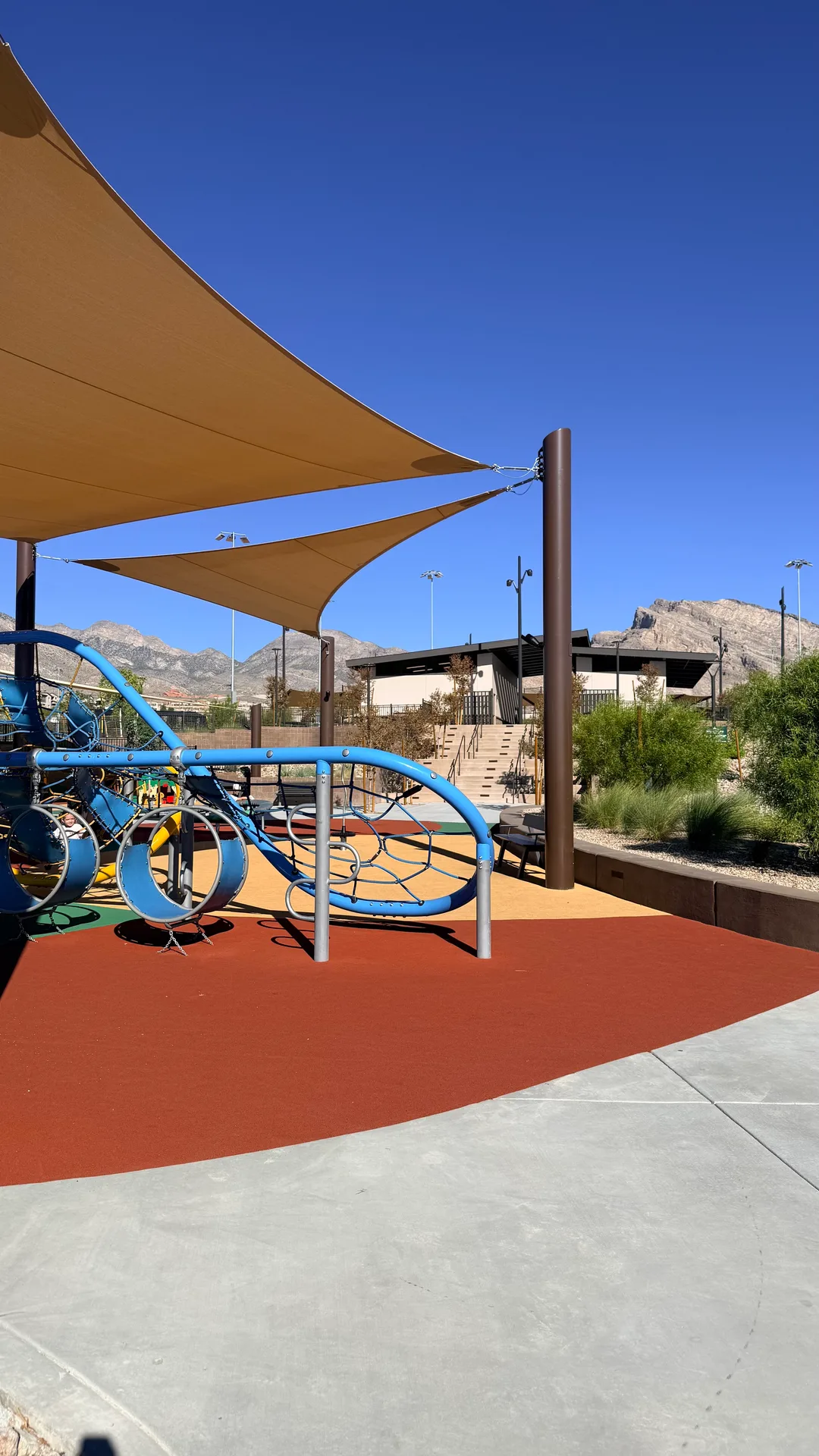 Grand Park playground with blue climbing equipment under large tan shade sails on soft rubber surfacing in Summerlin West
