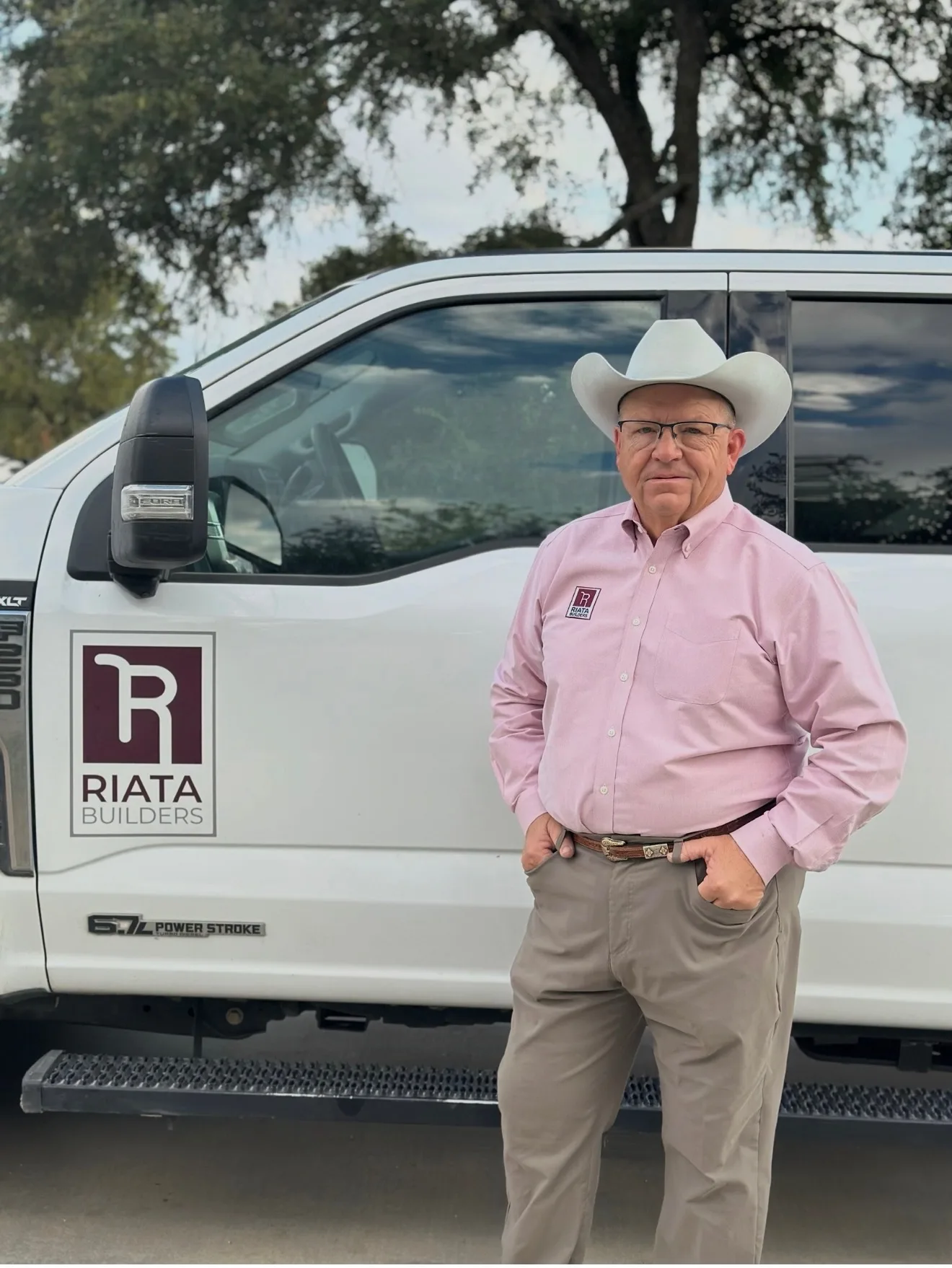 Jed Adams standing in front of his Riata Builders truck wearing a white cowboy hat