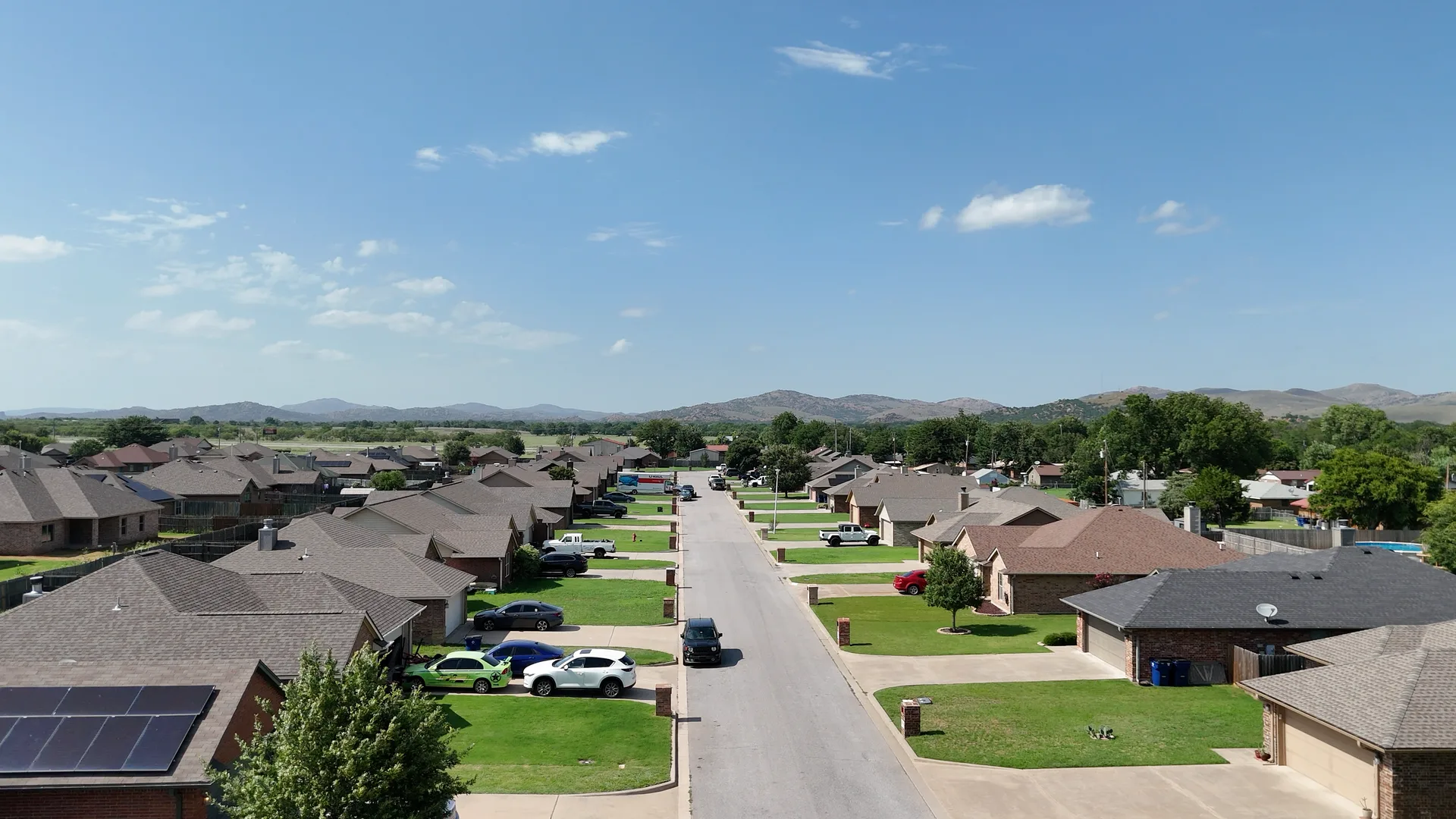 Aerial photo of a residential street lined with suburban single-family homes, with hills and mountains rising in the background