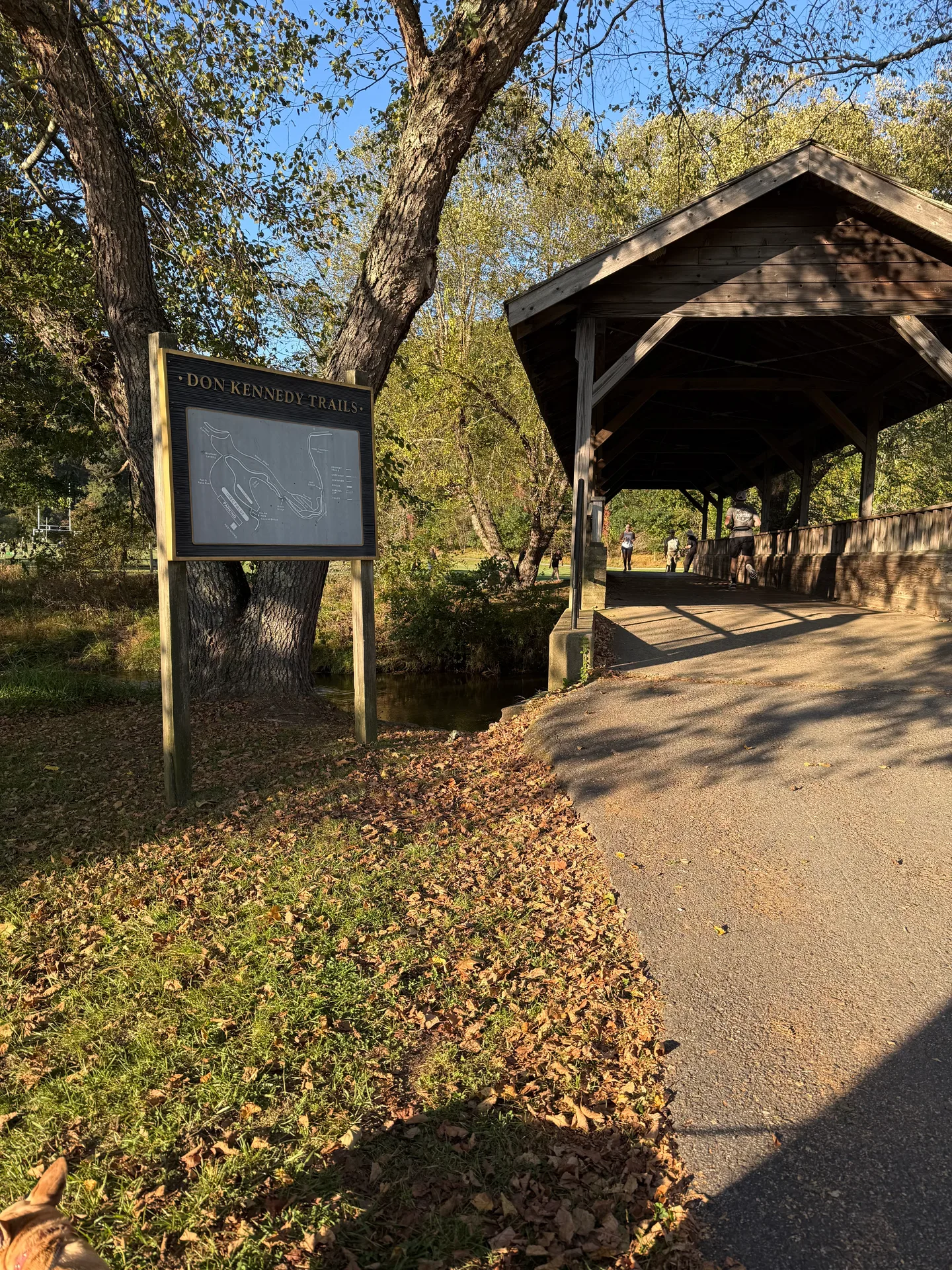 The Don Kennedy Trails entrance near Boone, a paved path through a wooden covered bridge with fall foliage and a trail map sign