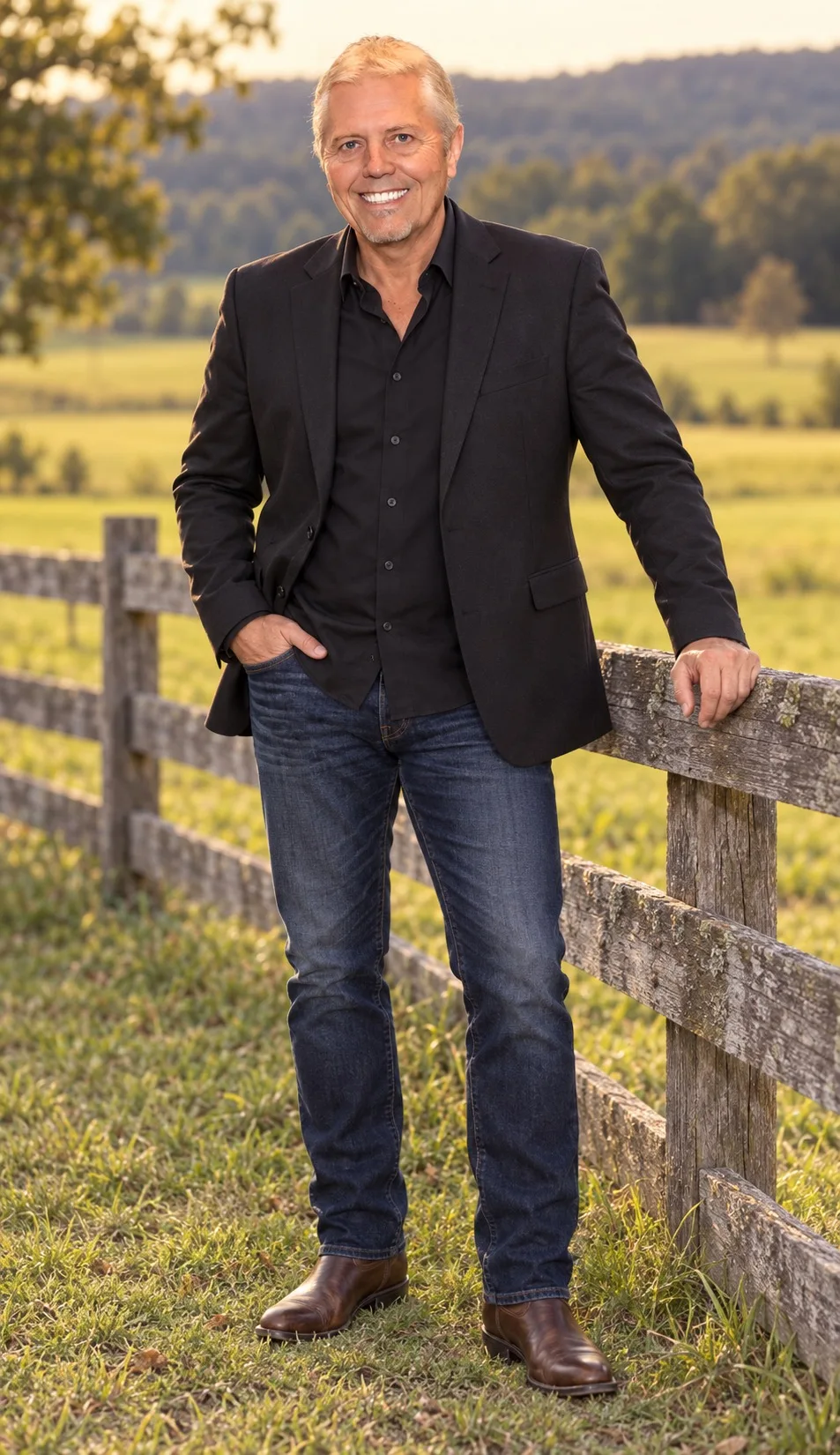 Mike Battistelli standing beside a rustic wooden fence in a field at golden hour