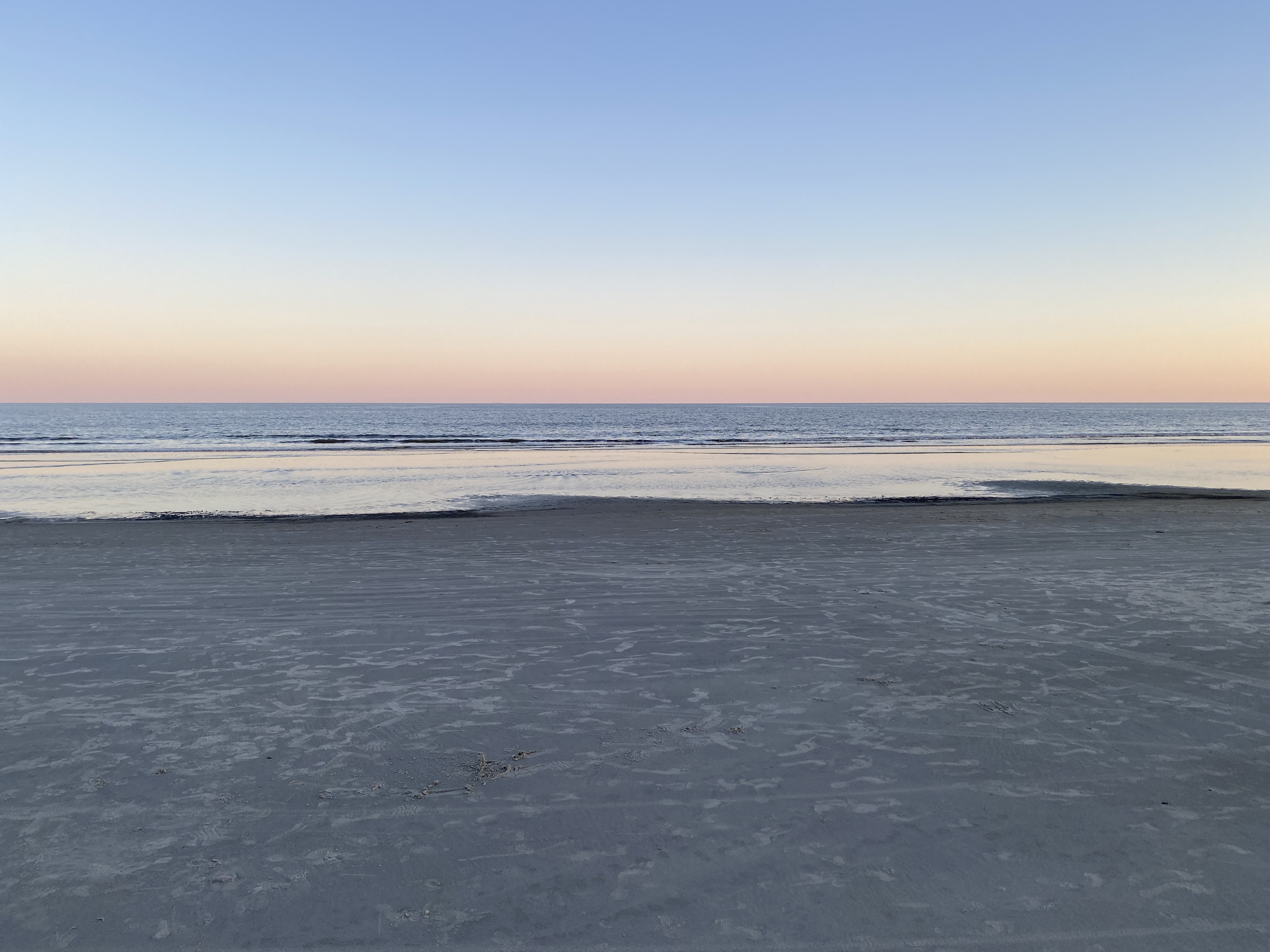 Calm empty beach on Hilton Head Island at sunrise, wet sand reflecting the soft pastel sky