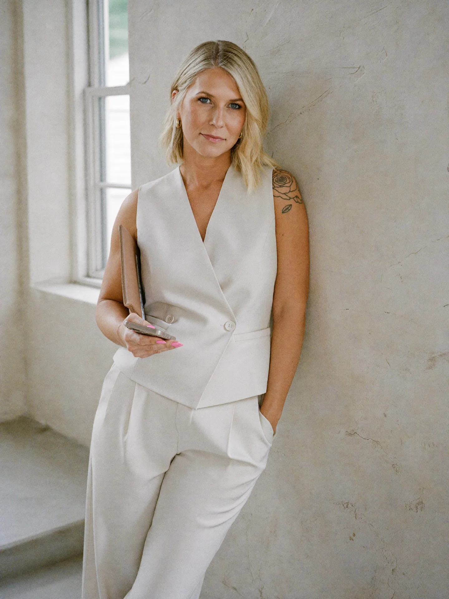 Nicole Elizabeth Yaeger in a cream vest leaning against a light wall in natural light