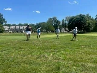 Golfers on the course with buildings in the background at the FORE the KIDS Golf Tournament