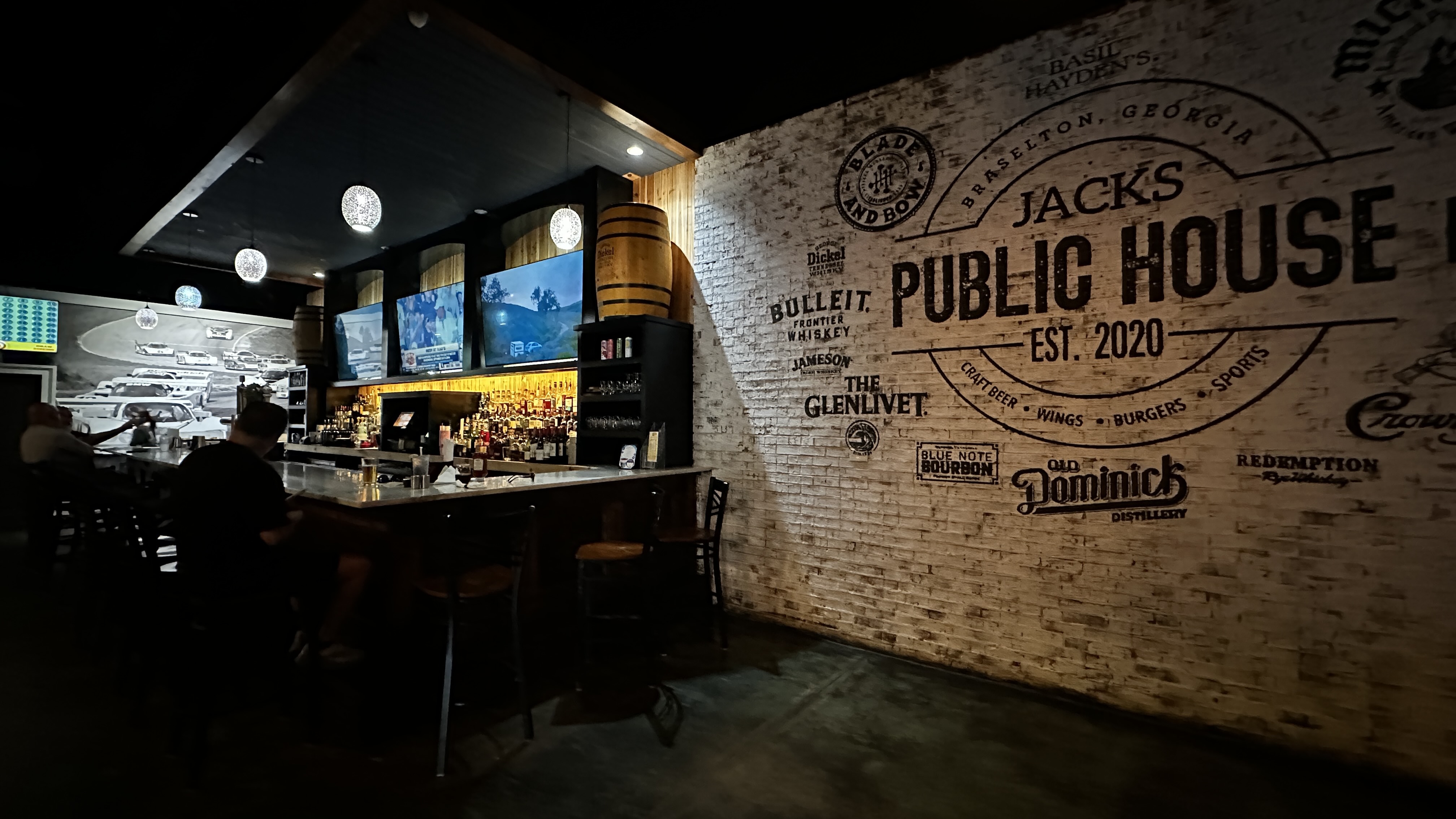 Bar area at Jack's Public House in Braselton Georgia with white brick Jack's logo mural bar stools and backlit liquor shelves
