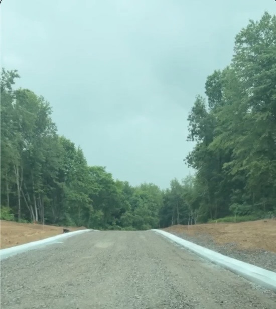 Aerial drone view of Oaks of Tyrone development in progress showing new concrete curbs being installed on gravel roads, wooded lots graded and prepared for construction in Tyrone Township, Michigan