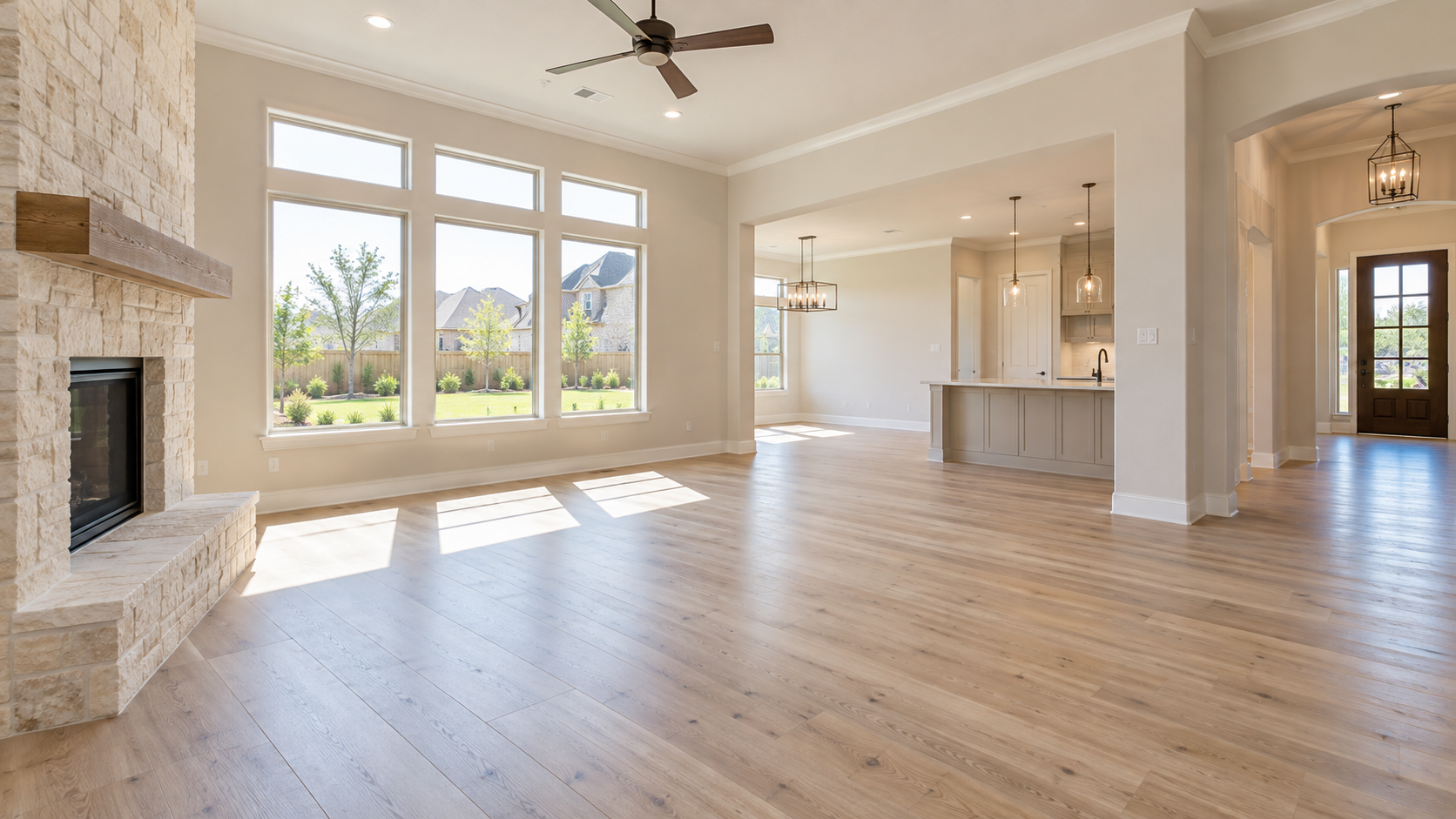 An unfurnished living room in a vacant home, with wide windows and natural light across an empty wood floor