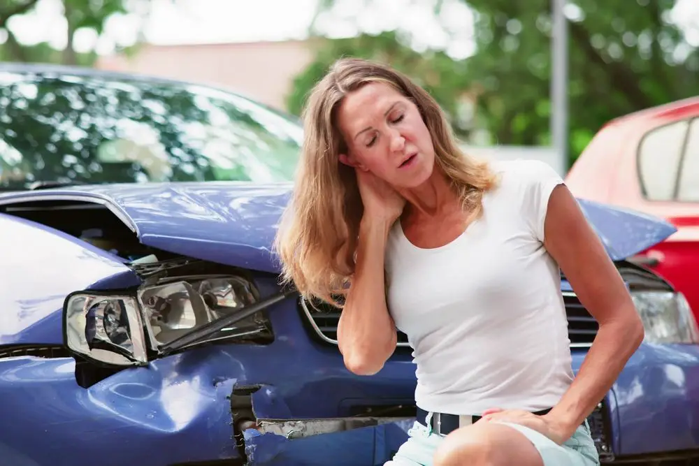 Woman holding her neck at a roadside accident scene after a collision
