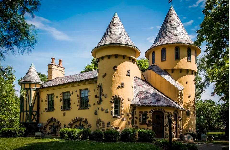 Curwood Castle in Owosso, Michigan — a whimsical stone Norman chateau-style castle with a round tower and turret on the banks of the Shiawassee River on a late summer afternoon