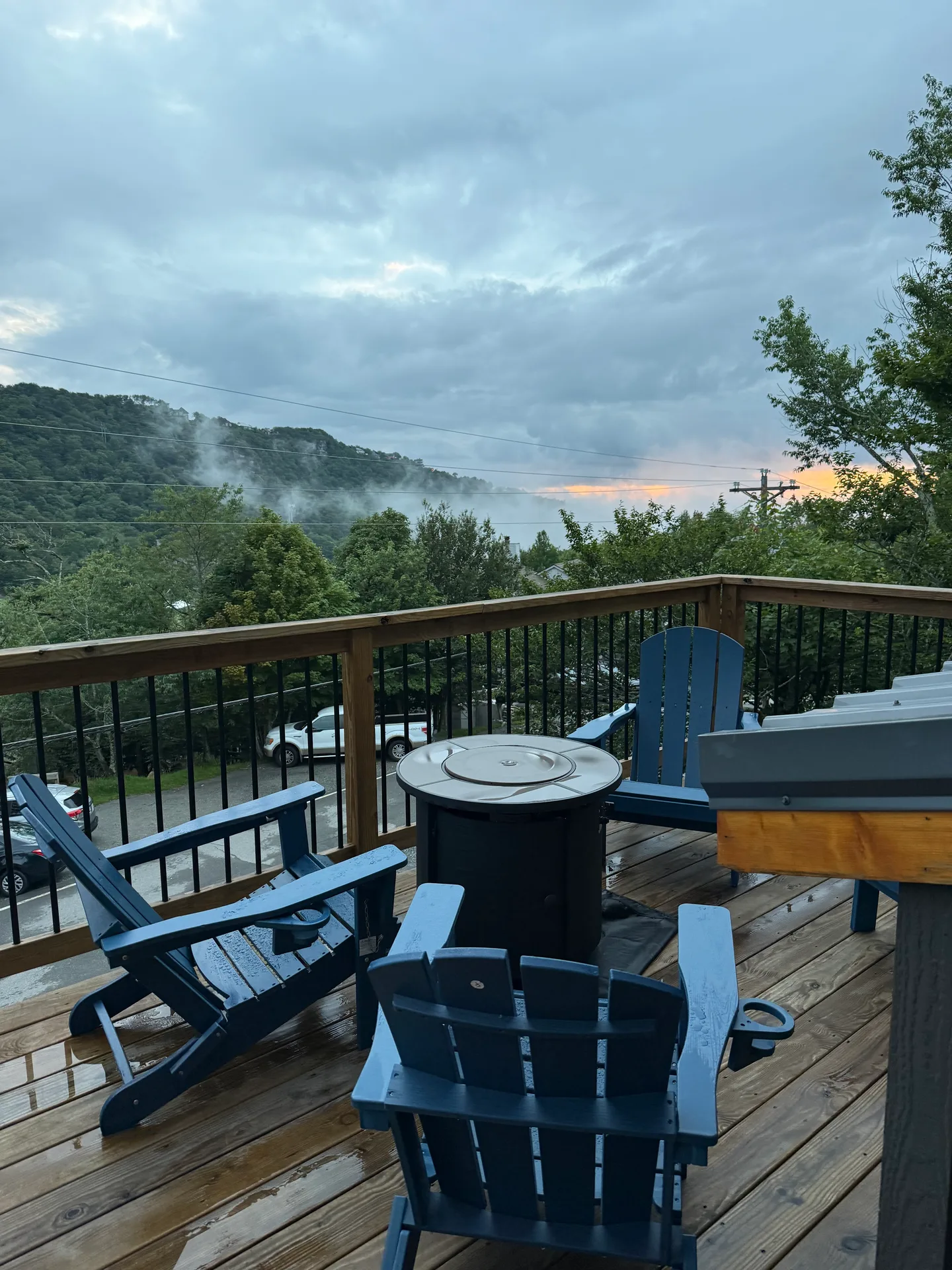 The cabin's back deck with blue Adirondack chairs around a fire pit, overlooking a misty forested mountain landscape at sunrise