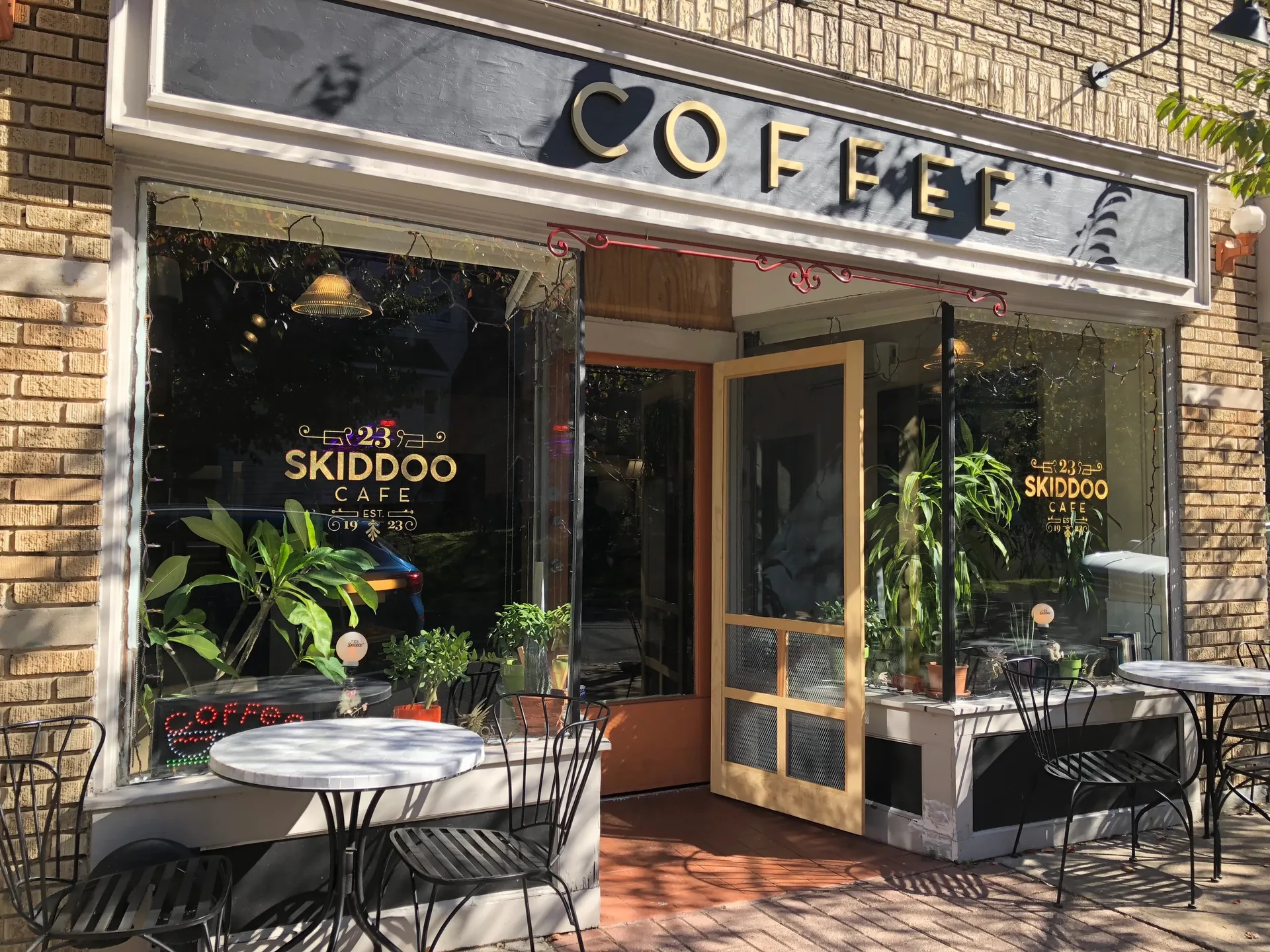 Daytime exterior of the 23 Skiddoo Cafe storefront in Bloomfield's Watsessing neighborhood, brick facade with a COFFEE sign and bistro tables outside