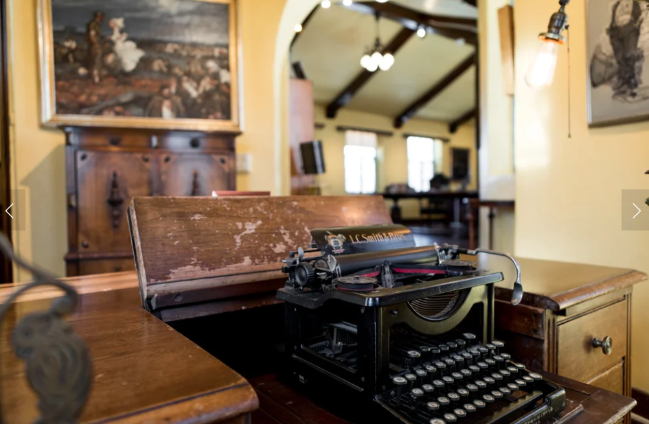 Cozy writing studio interior of Curwood Castle with James Oliver Curwood's original desk, chair, and shelves of vintage books in warm amber lamplight