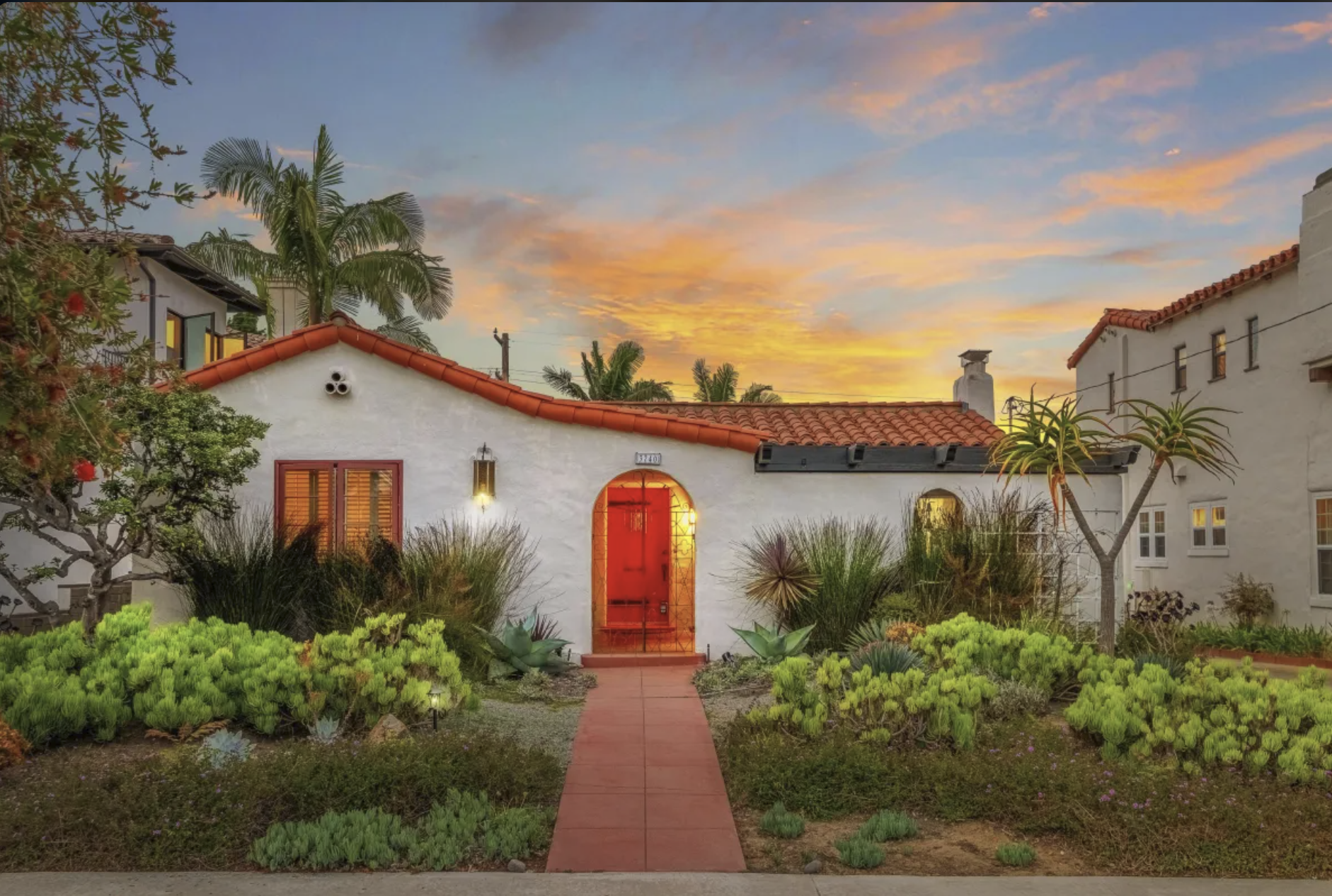 Spanish Colonial style single-story home with white stucco, red-tiled roof, and a red front door at sunset