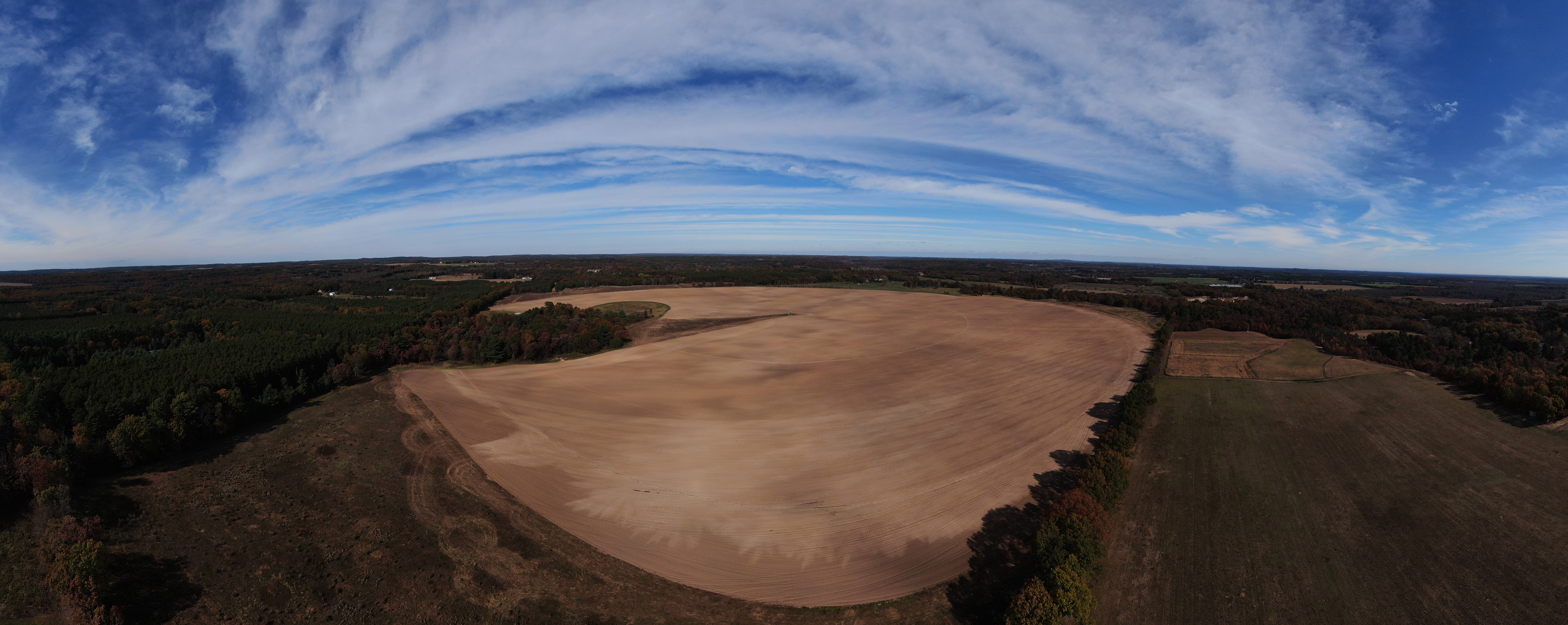 Aerial view of agricultural farmland with plowed fields, forests, and open Wisconsin sky