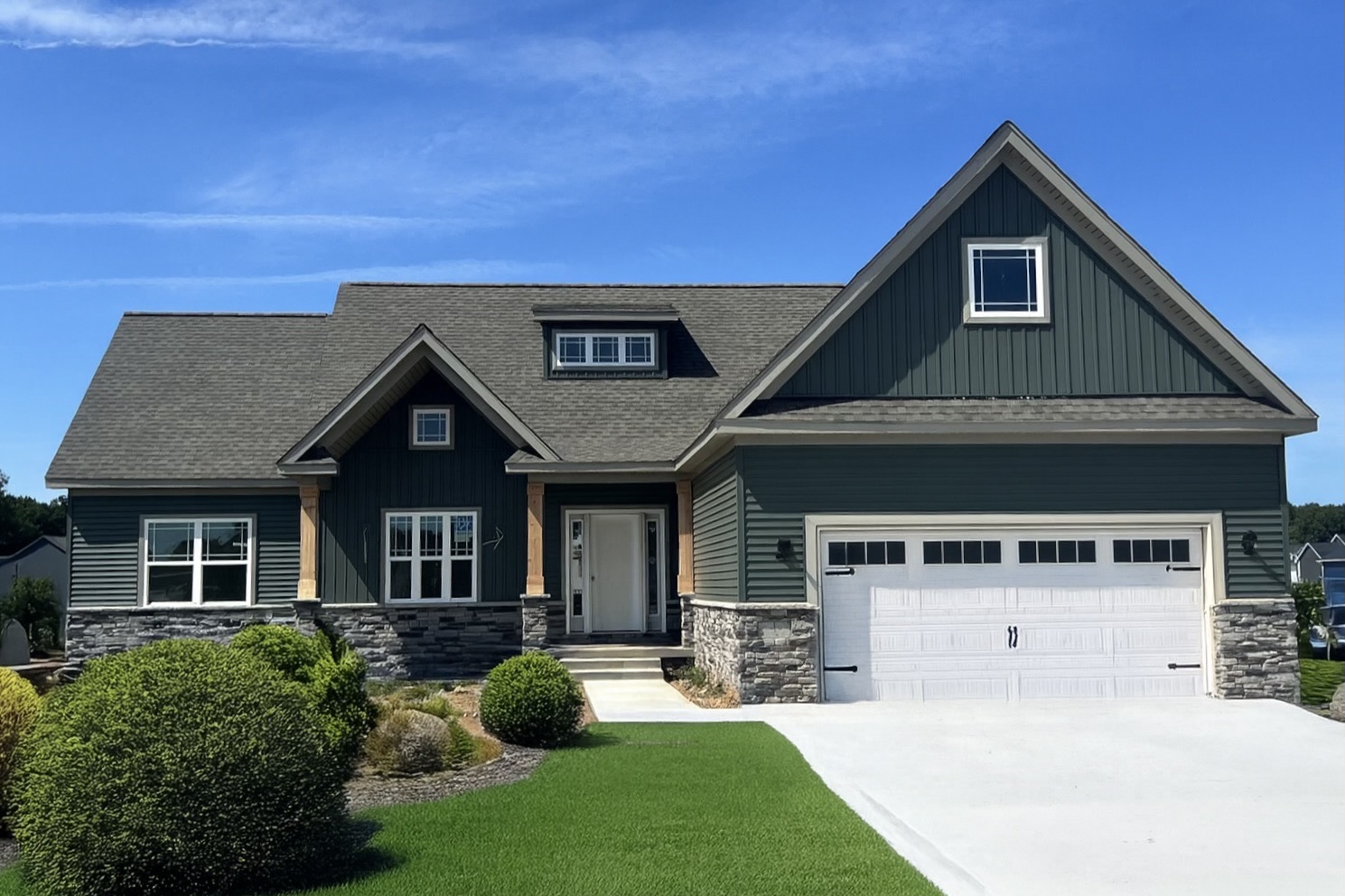 Big Sky Development custom home with dark teal green siding, stone veneer accents, wooden porch posts, and white garage door