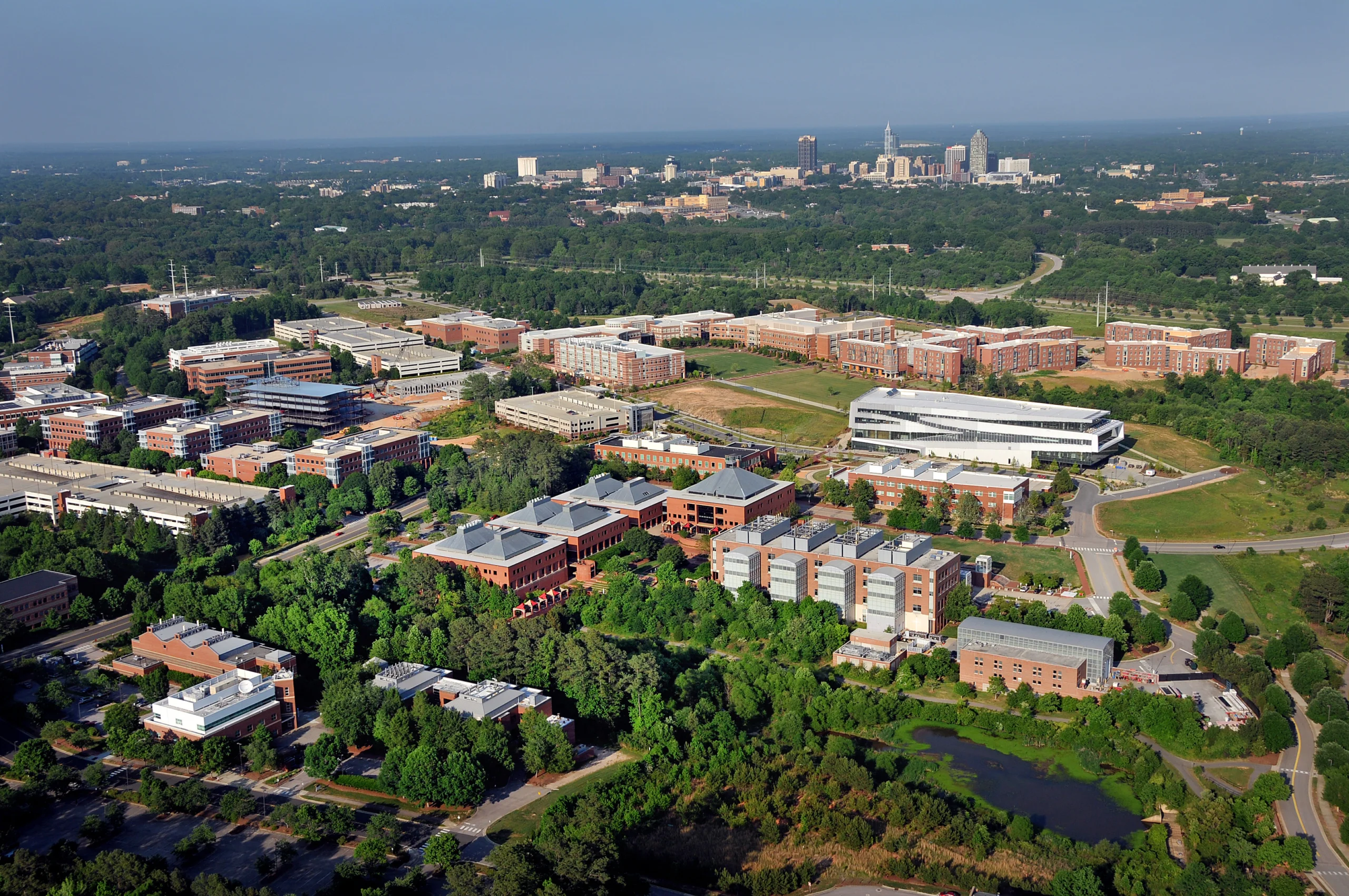 Aerial view of Research Triangle Park with office buildings, green space, and a distant city skyline, a short commute from Forest Hills