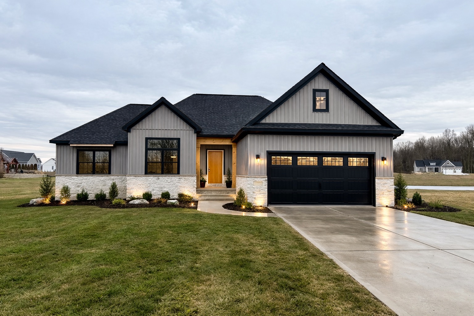 Modern Farmhouse exterior at dusk by Big Sky Development with grey siding, stone veneer, landscape lighting, and black garage doors