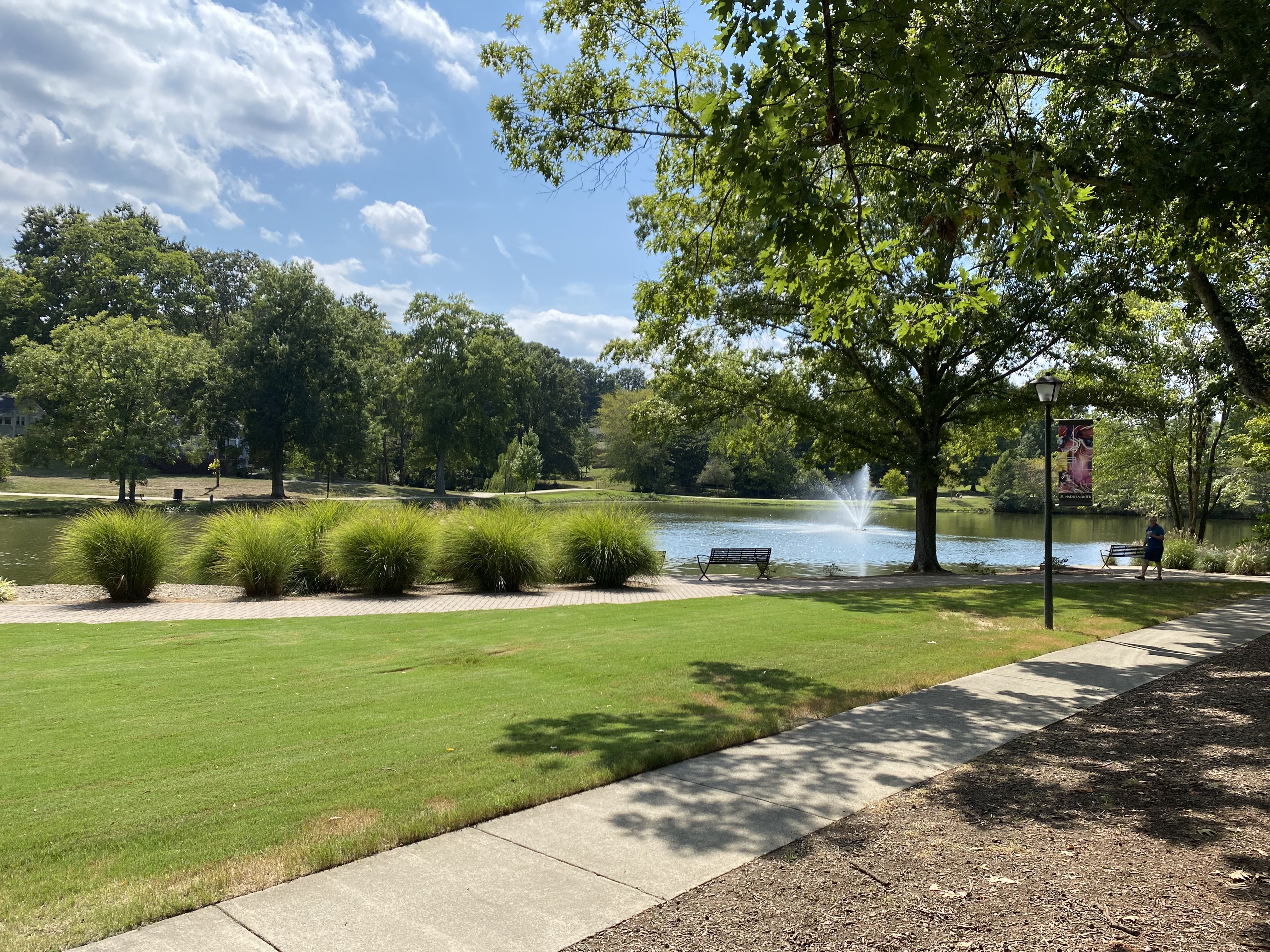 Iconic Davidson village pond and fountain surrounded by lush green trees and parkland with the town green visible in the background on a sunny afternoon