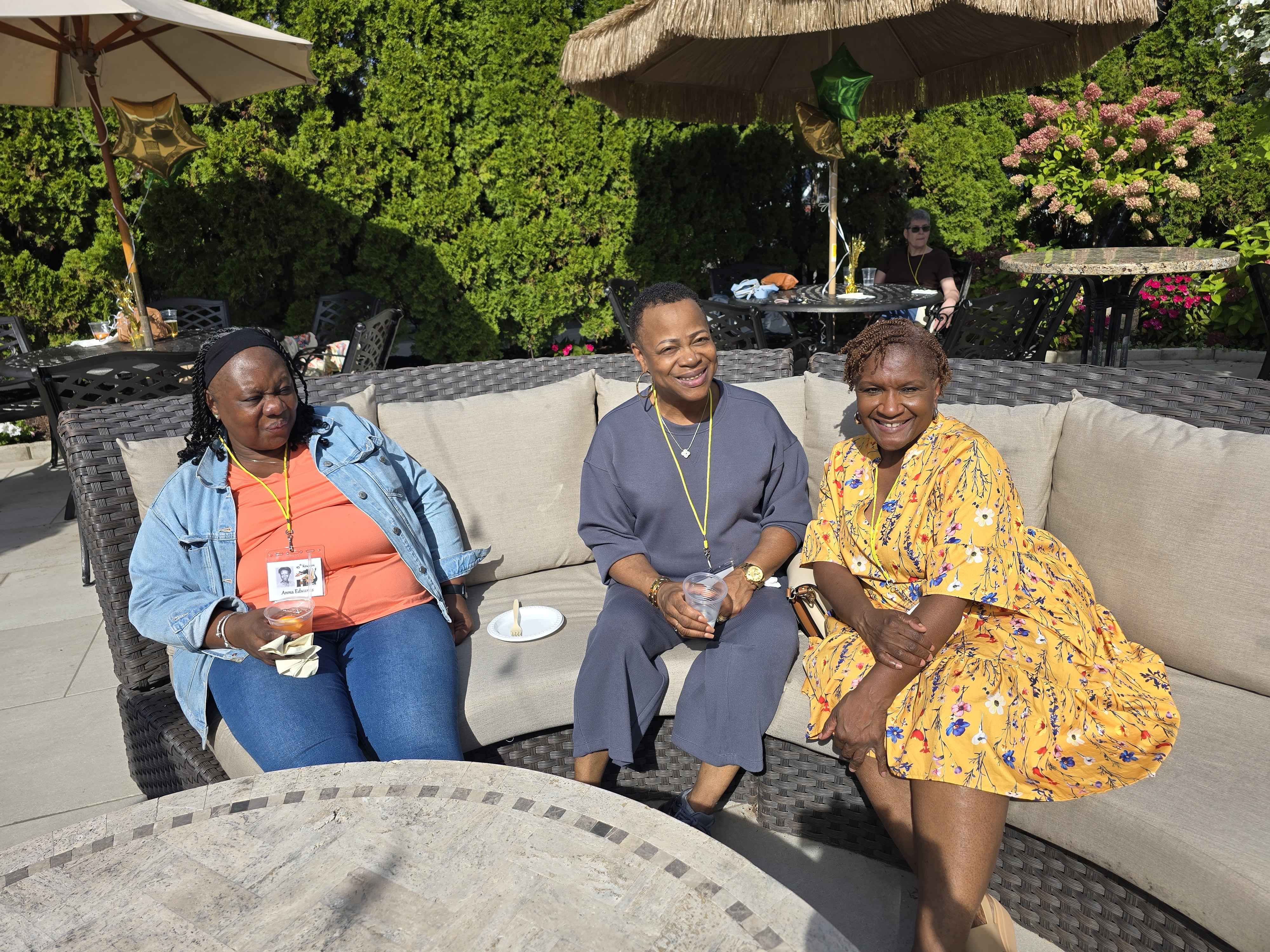 Three smiling women wearing name tags and holding drinks on a sunny outdoor patio at the Hamden High Class of 1981 45th reunion.