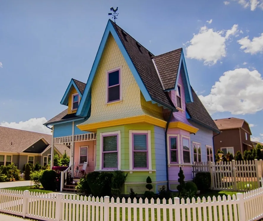 The real-life Up house in Herriman, Utah, with its colorful yellow, blue, and green siding, white picket fence, front porch, and rooster weather vane