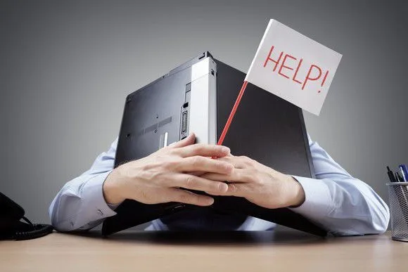 Person at a desk with a laptop and a small HELP! flag, illustrating how overwhelming selling a home can feel