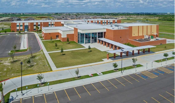 Aerial view of a red-brick school campus with classroom buildings, sports fields, and surrounding green grounds