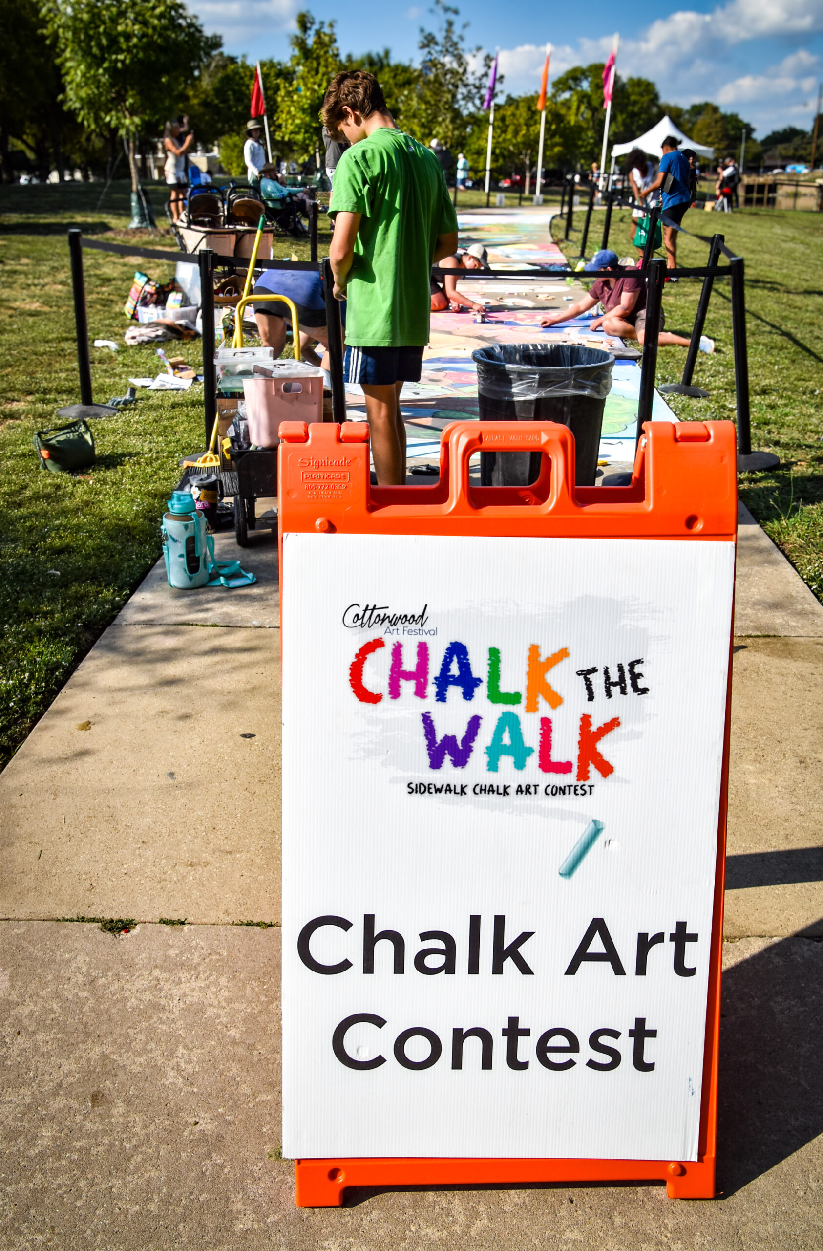 Artists creating sidewalk chalk art along a sunny festival walk at the Cottonwood Art Festival, with visitors gathered around the chalk artwork.