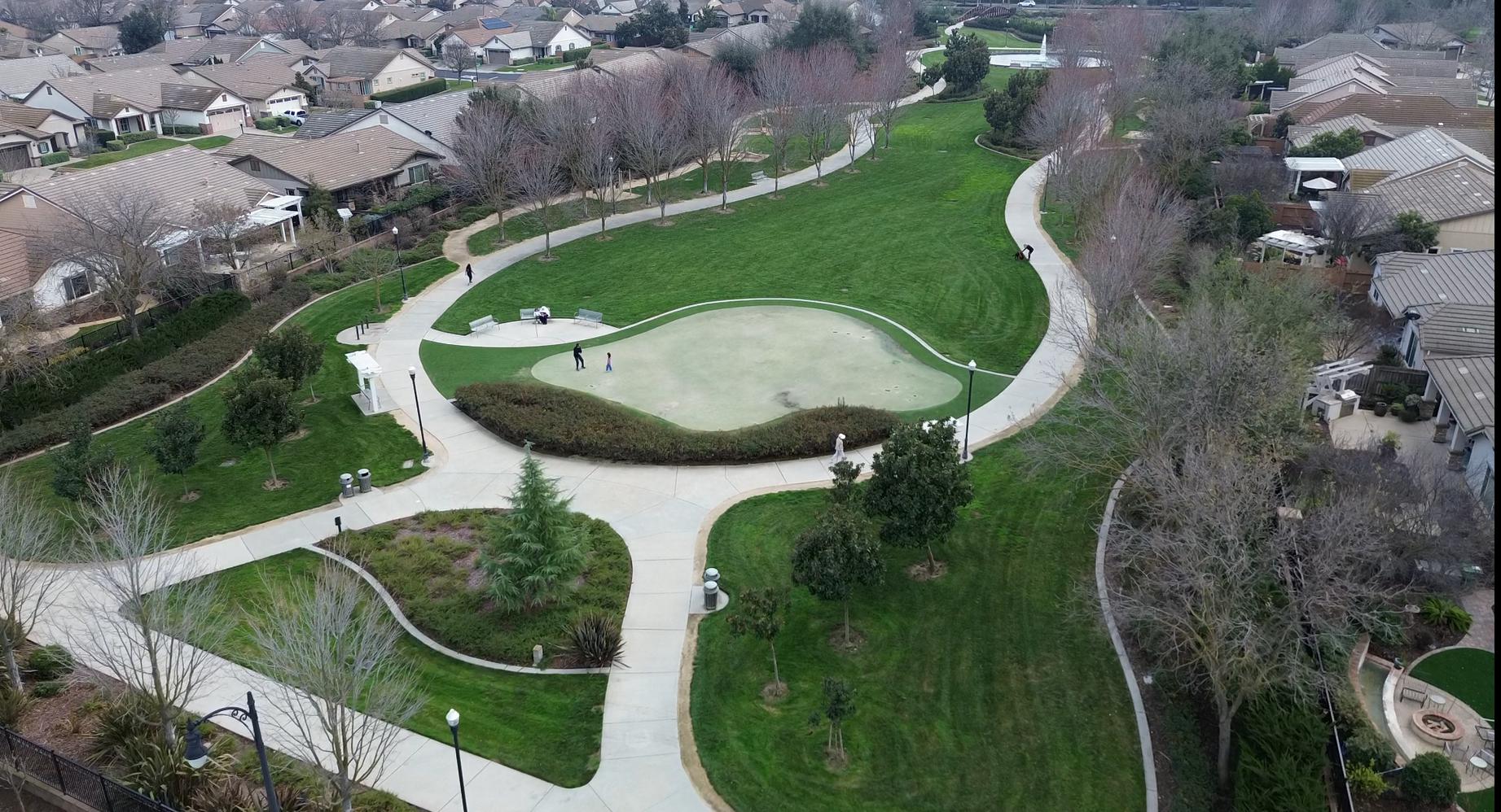 A resident practicing putts on the putting green at Del Webb Glenbrooke in Elk Grove, with residents walking the paths nearby