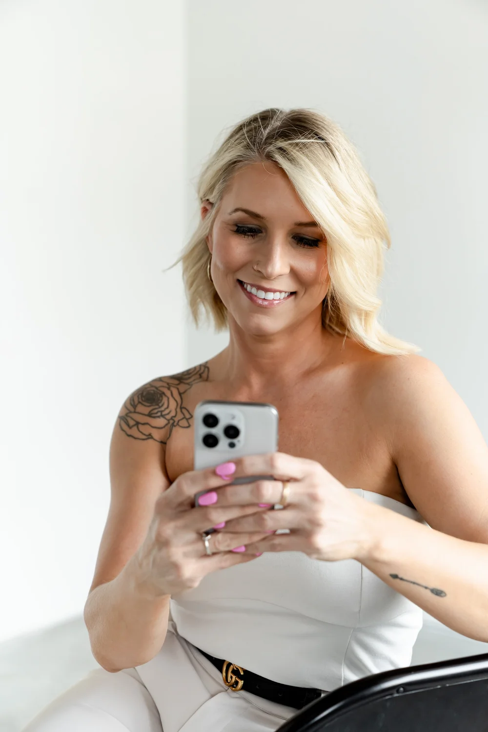 Nicole Elizabeth Yaeger in a white outfit with a gold belt, smiling at her phone