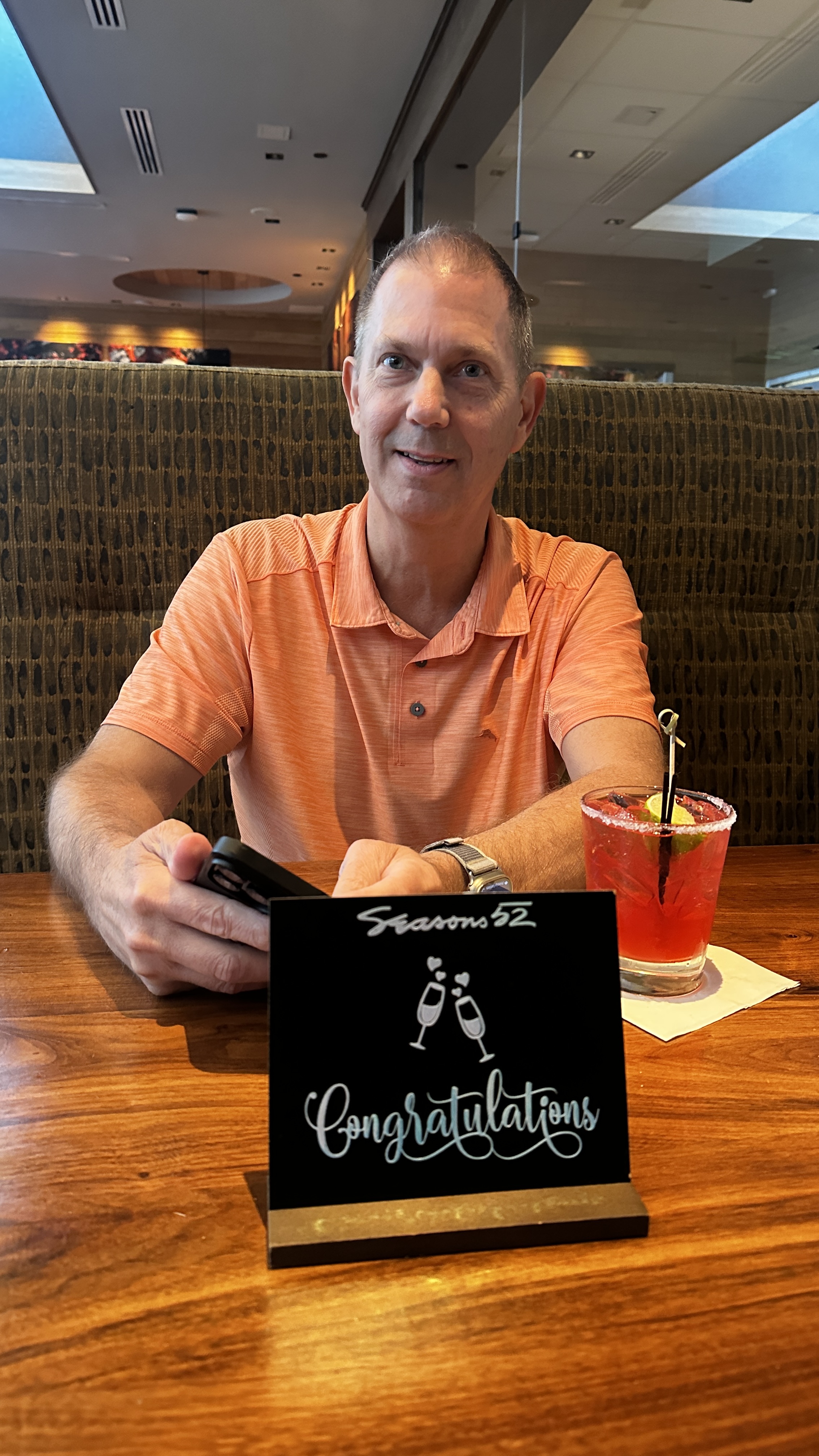 Alan Boyd holding a Congratulations sign and cocktail at Seasons 52 restaurant in Buford Georgia