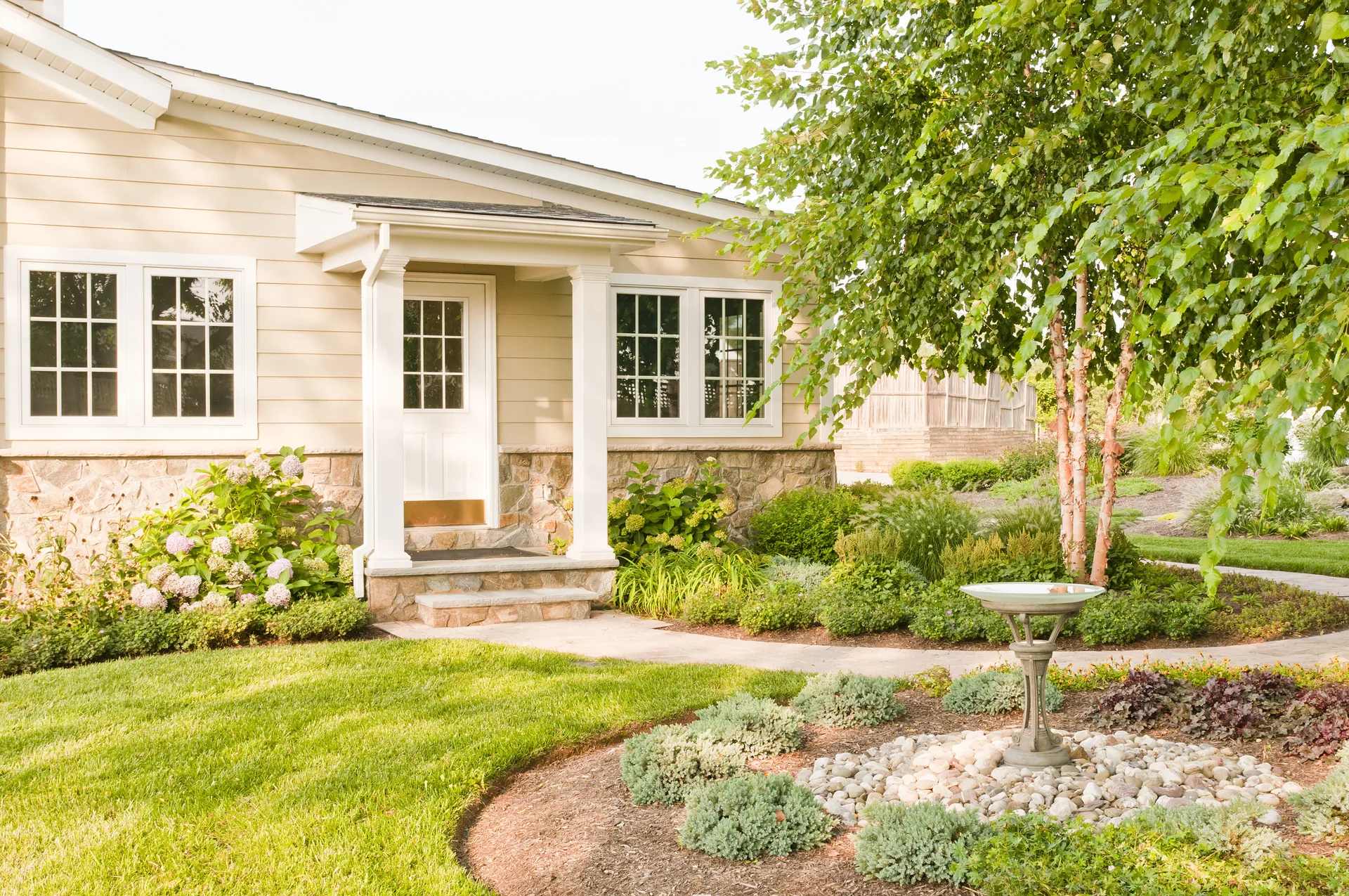 Light tan home with white trim, stone accents, and a covered porch in a landscaped front yard