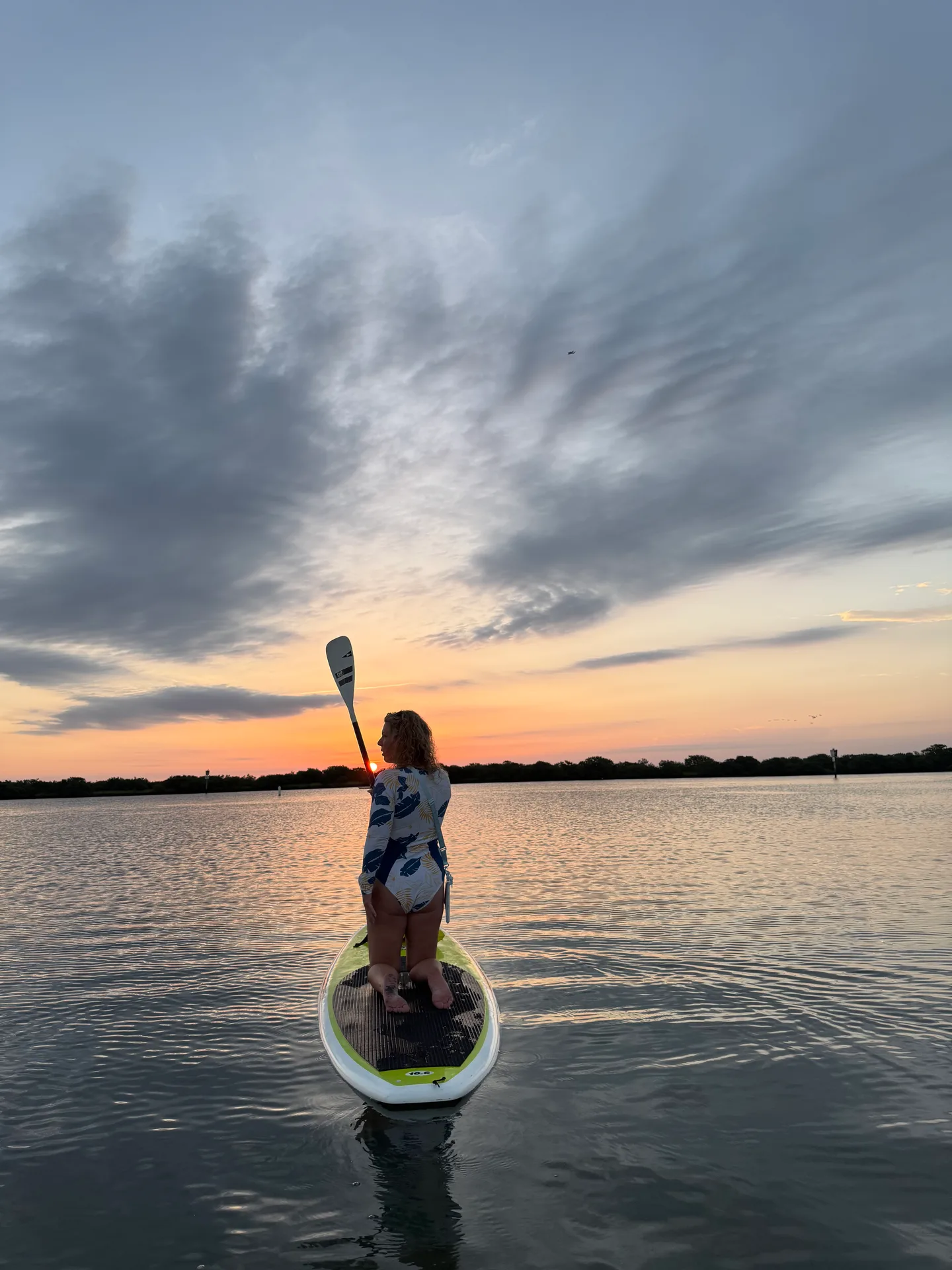 A paddleboarder kneeling on calm water at sunset near the Nocatee paddle launch