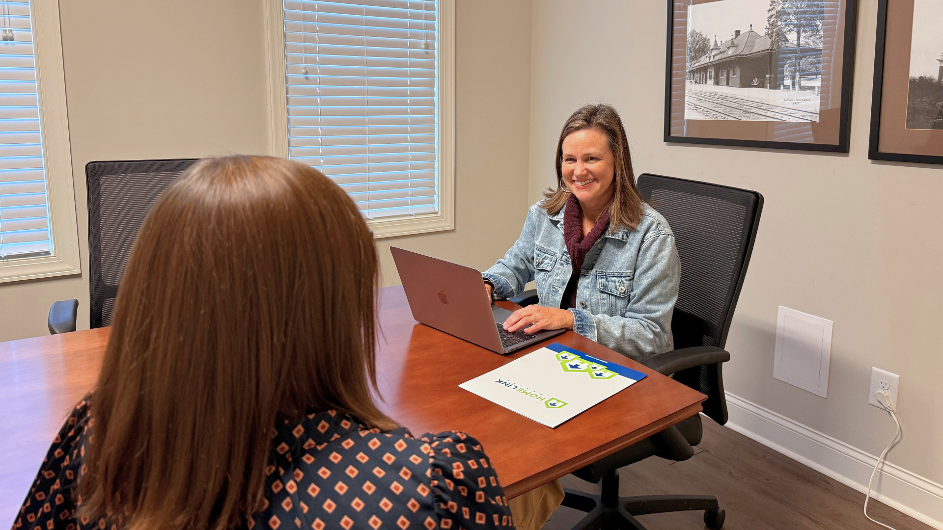 Over-the-shoulder view of a seller consultation, client working on a laptop with a HomeLink folder on the desk