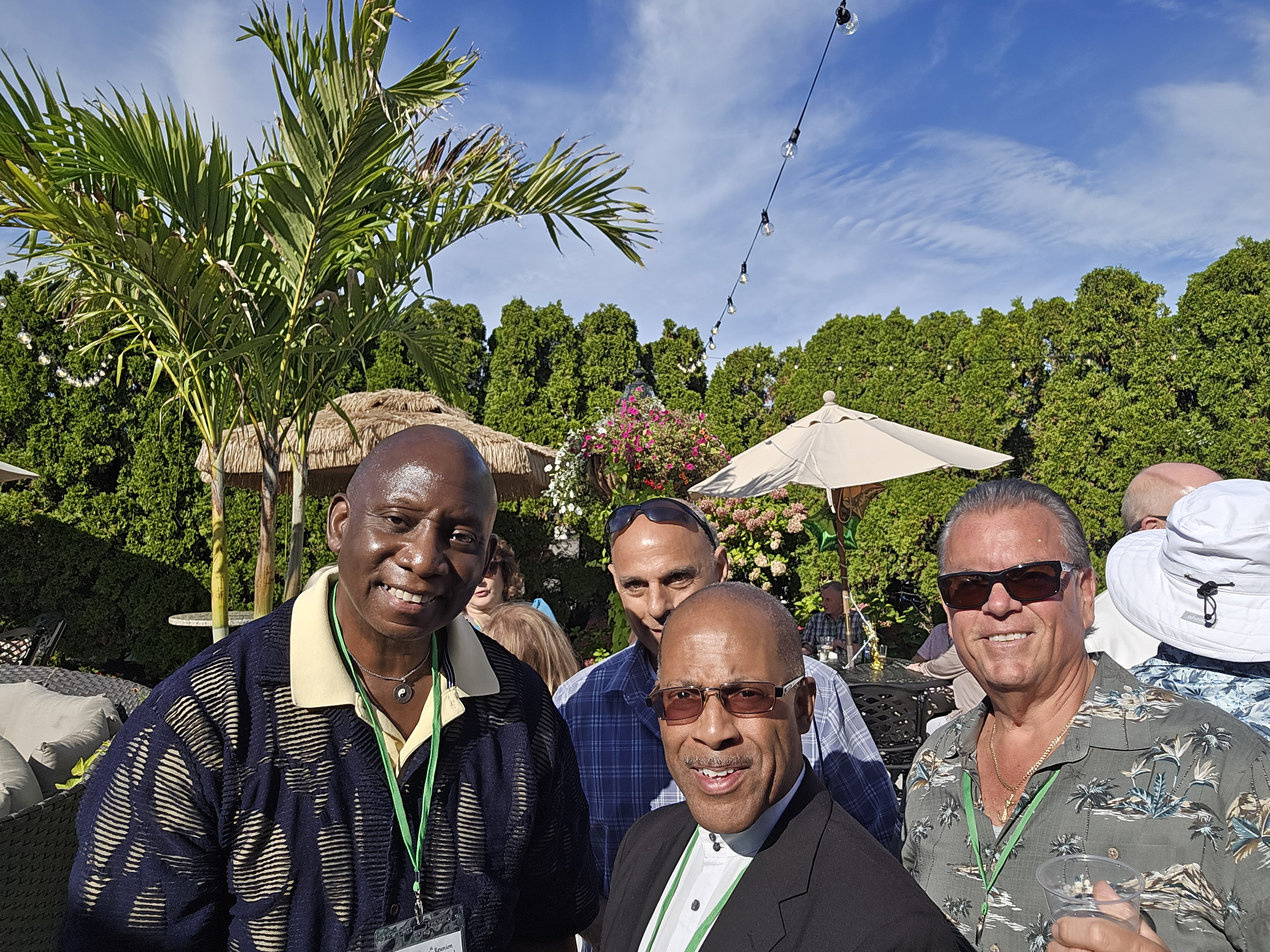 Four men smiling and posing together on the patio, all wearing green lanyards with reunion name tags at the Hamden High Class of 1981 45th reunion.