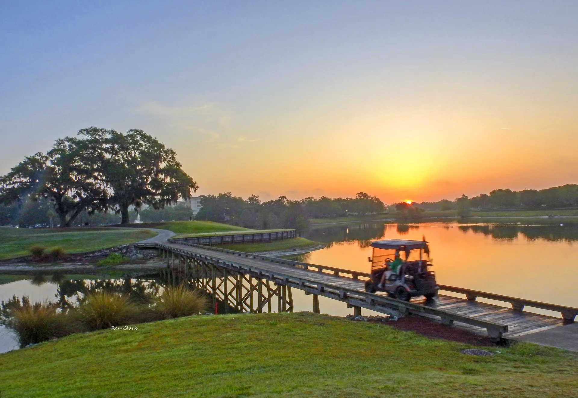 A golf cart crosses a wooden bridge over a pond during a golden sunset at a Florida golf course