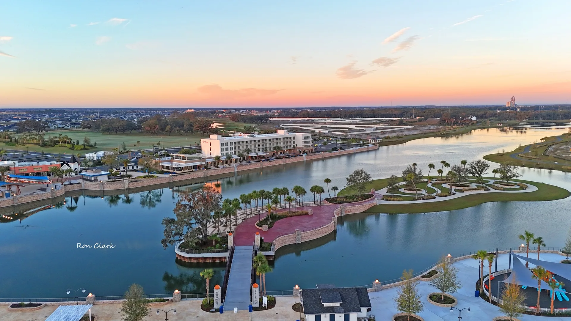 An aerial drone view of a waterfront Florida community with a lake, bridge, and walking paths at sunset