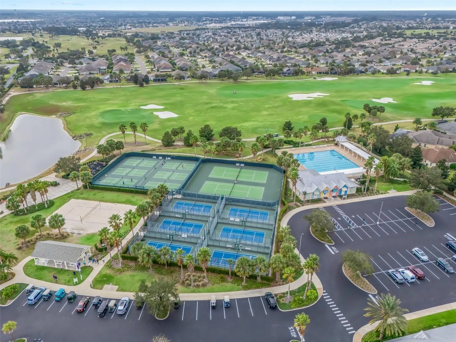 An aerial view of a Florida community with pickleball and tennis courts, a pool, and fairways