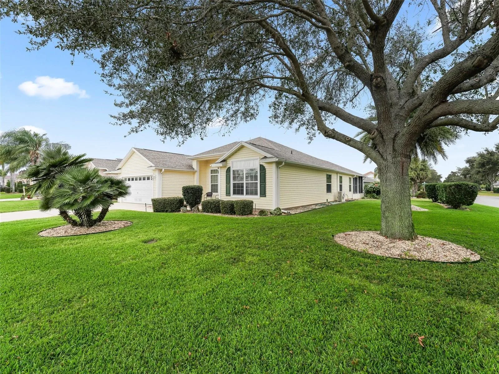 A pale yellow single-story Florida home with a green lawn and large shade trees