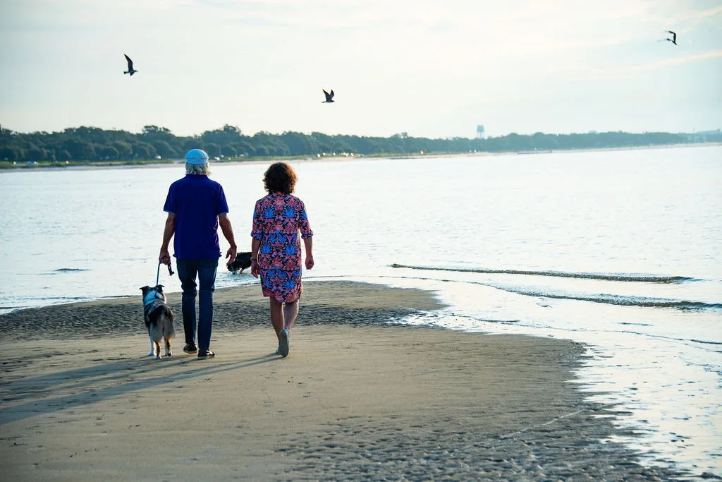 A man and woman walk with two dogs along the beach shoreline during the daytime on the Mississippi Gulf Coast