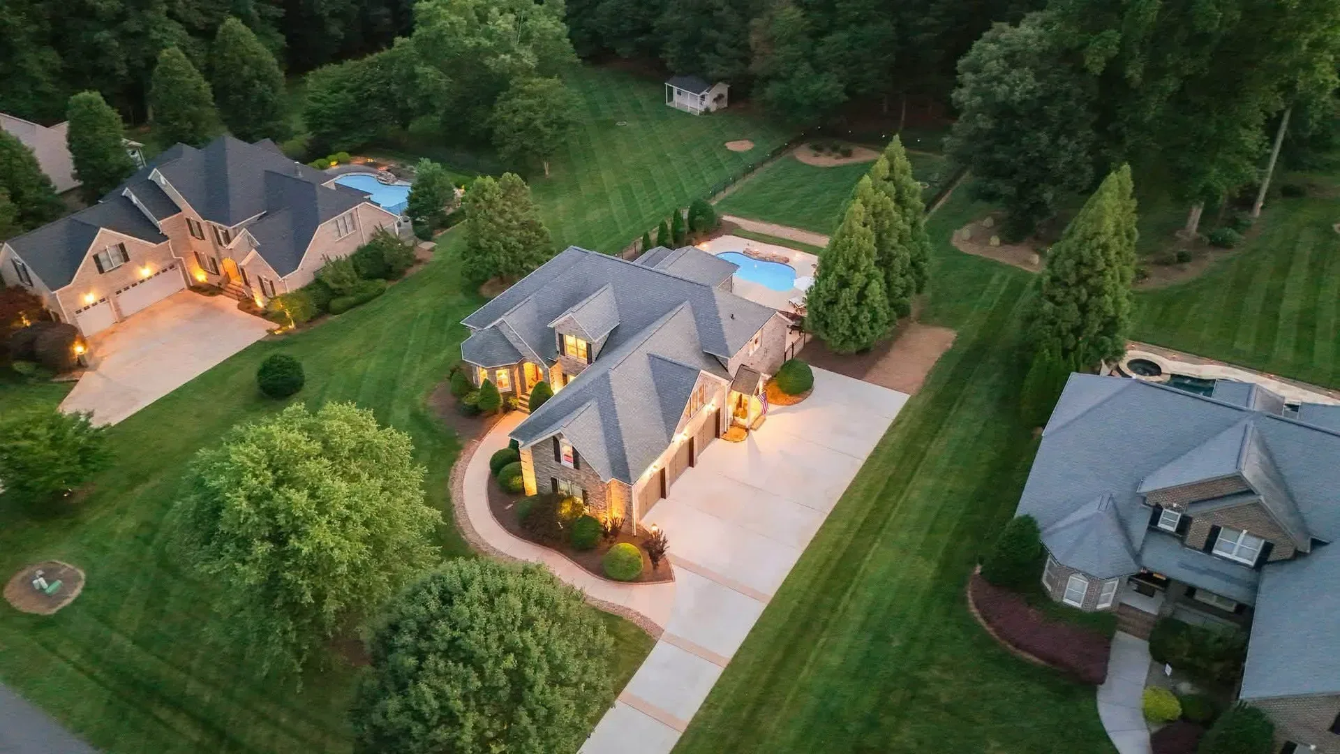 Aerial view of an upscale Lake Norman neighborhood at dusk with houses, pools, and warm evening lights