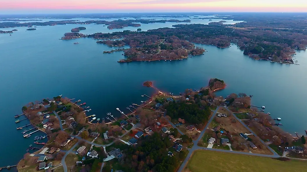 Aerial drone shot of Lake Norman residential lake community at dusk with houses along the shoreline, private docks, and sunset reflecting across the water