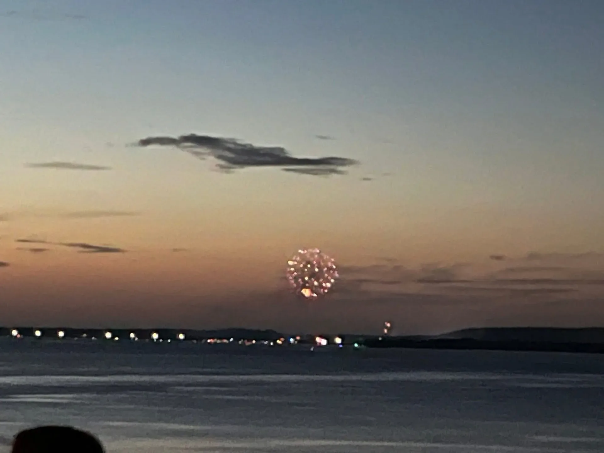 A single firework bursting over dark water against a dusk sky