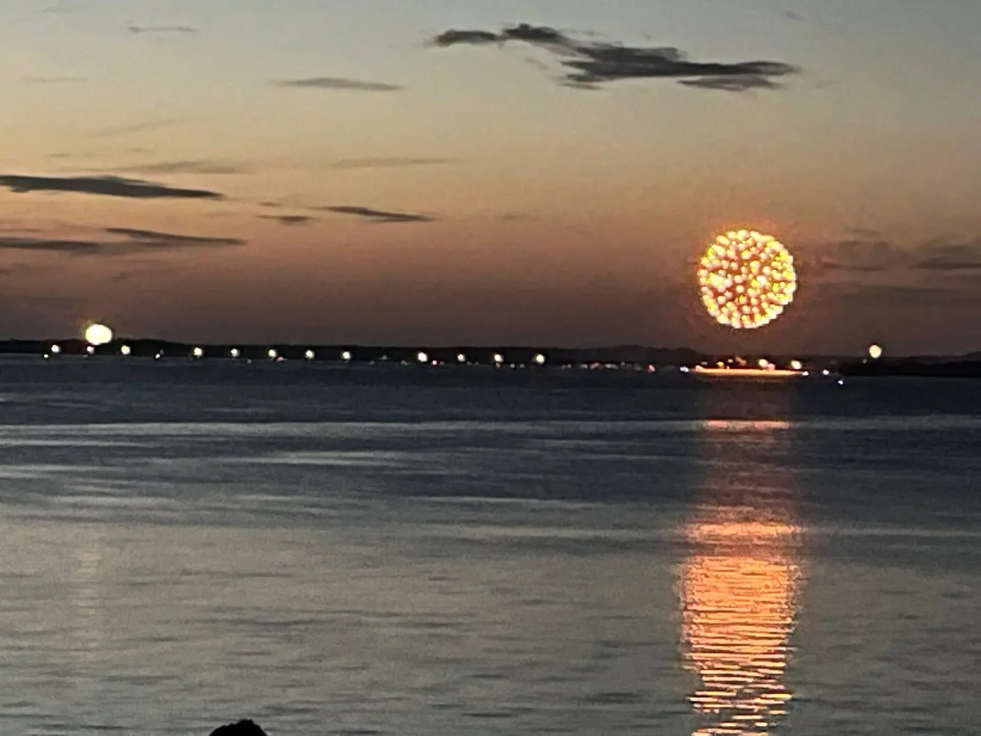 Fireworks bursting over dark water at twilight with reflections on the lake